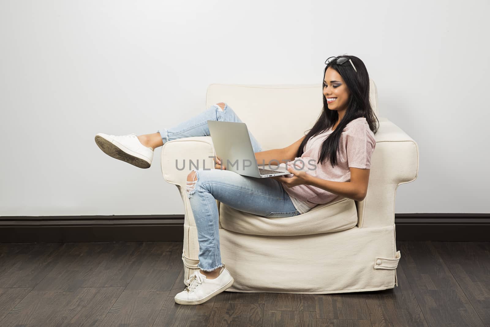 twenty something woman working on a grey laptop, with one leg up on the arm of the couch
