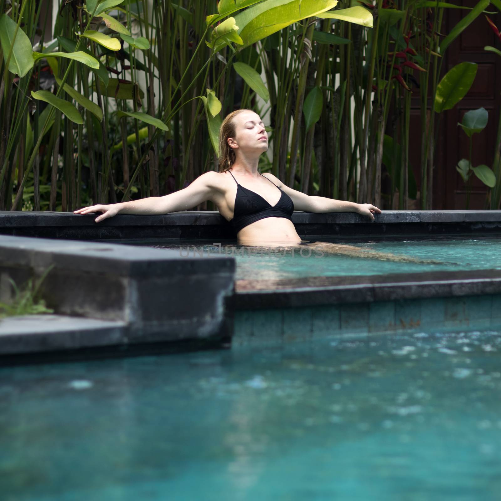 Sensual young woman relaxing in outdoor spa infinity swimming pool surrounded with lush tropical greenery of Ubud, Bali. by kasto