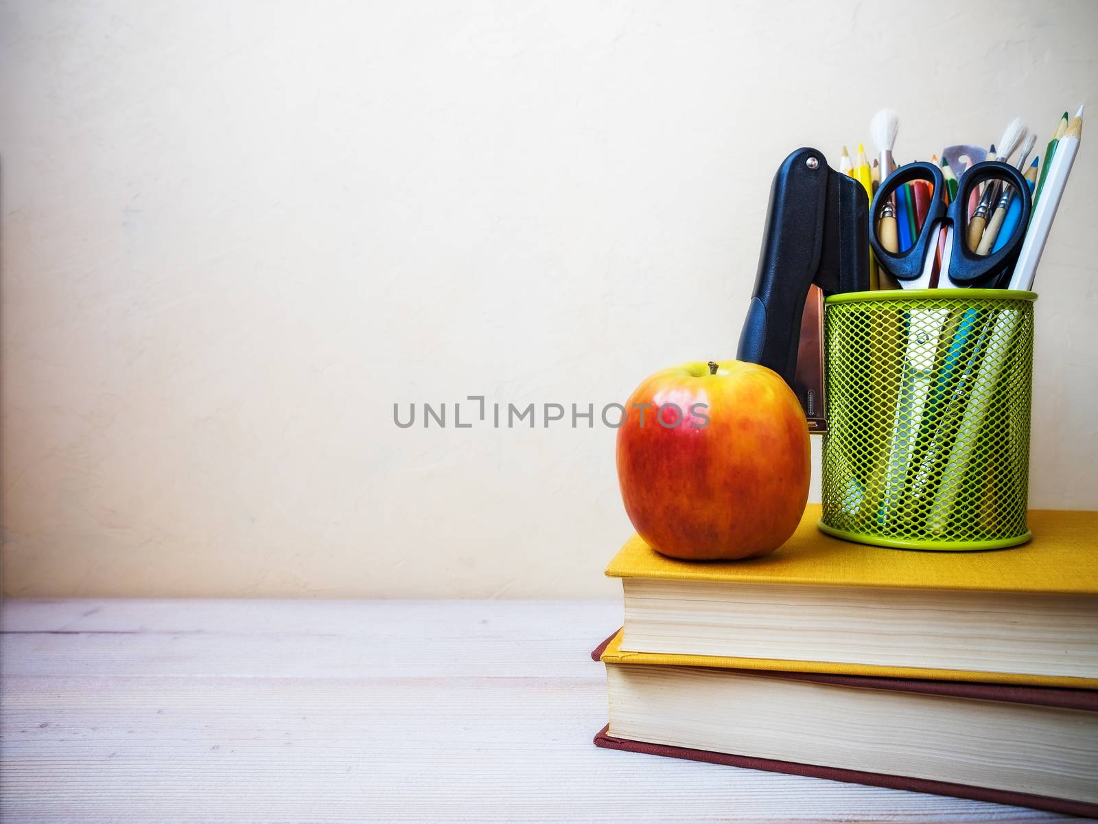 View on the pile of books, apple and cup with pencils lying on the wooden table