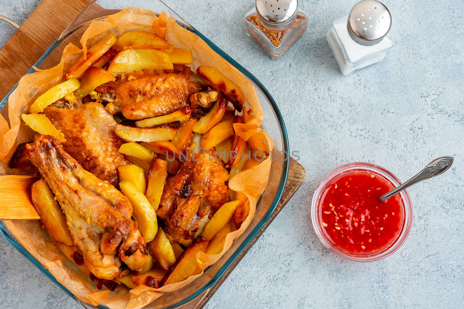 Baked turkey wings with potato pieces in a square baking dish on a gray kitchen table with sauce and spices - photo, image by galsand