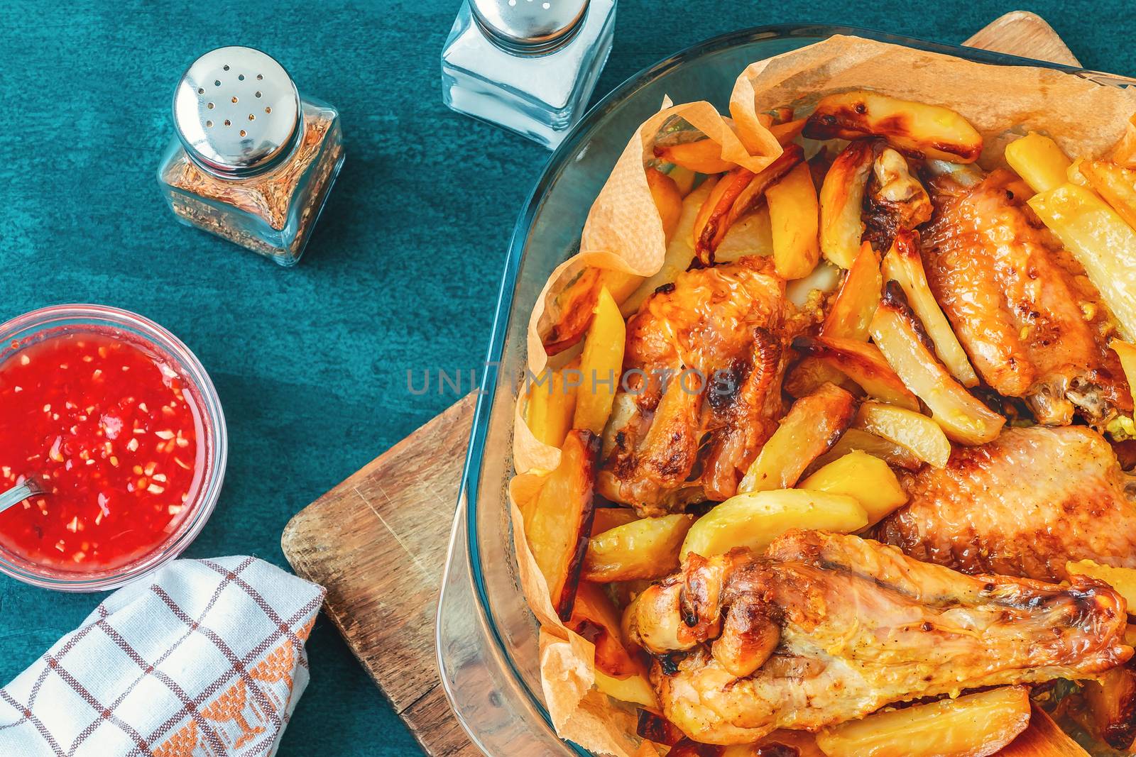 Baked turkey wings with potato pieces in a square baking dish on a turquoise kitchen table with sauce and spices - photo, image.