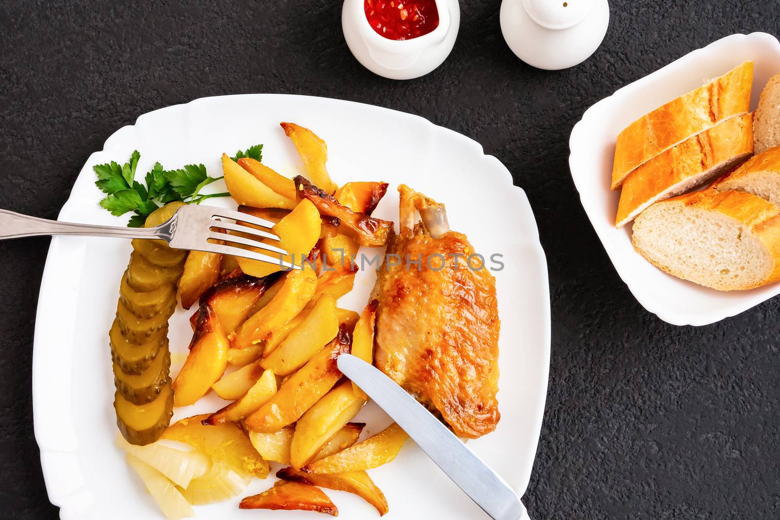 Baked turkey wings with potato pieces on a white plate on a black kitchen table with tartar sauce and tomato sauce and spices - photo, image by galsand