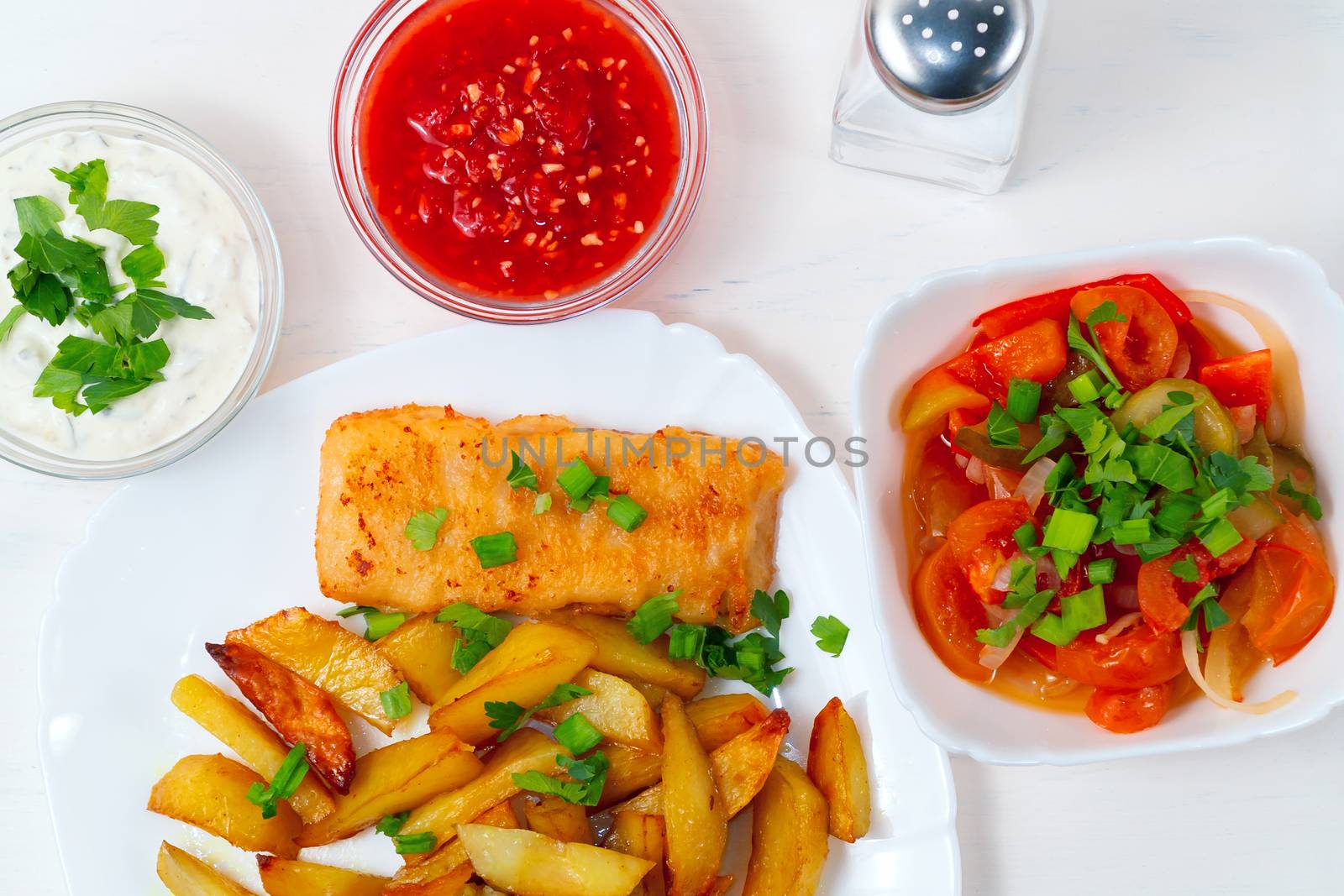 Fried fish and chips on a white plate on the white kitchen table with tomato sauce, tartar sauce and pickled vegetables salad - photo, image. by galsand