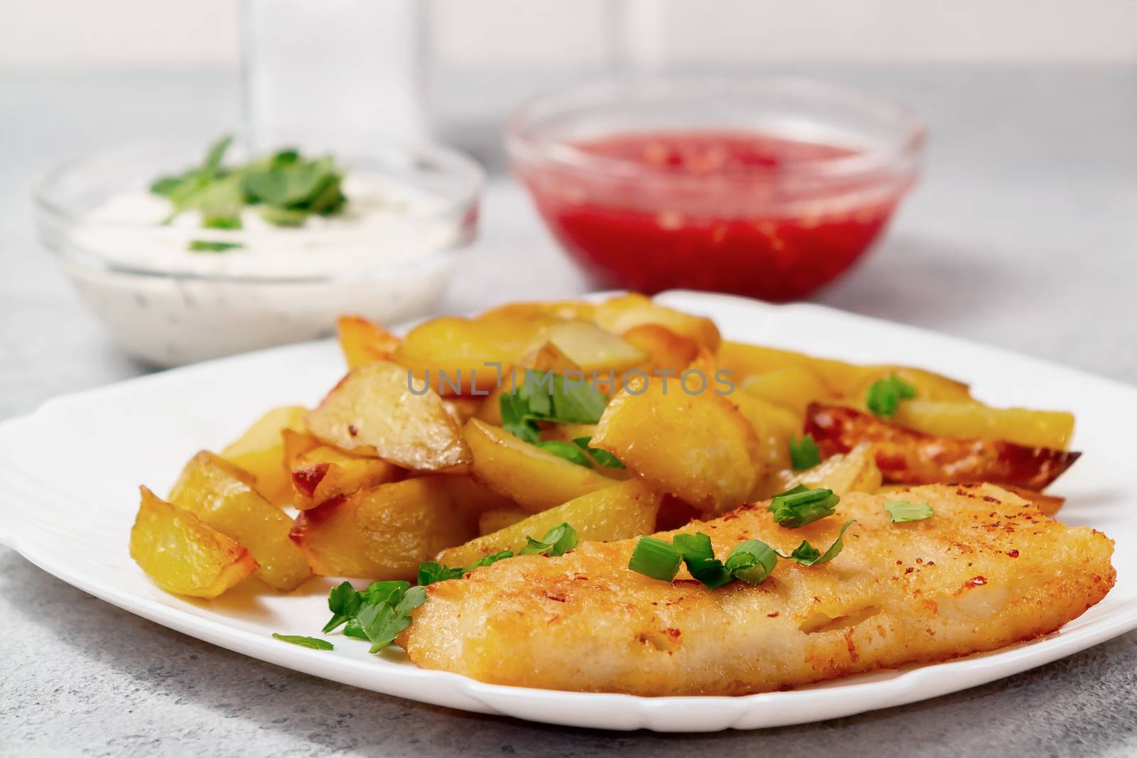 Fried fish and chips on a white plate on the kitchen table with tomato sauce, tartar sauce and pickled vegetables salad - photo, image.