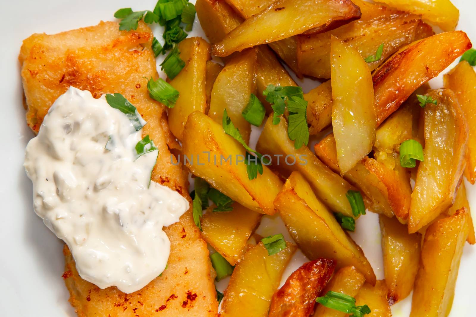 Fried fish and chips on a white plate on the kitchen table with tartar sauce close-up - photo, image by galsand