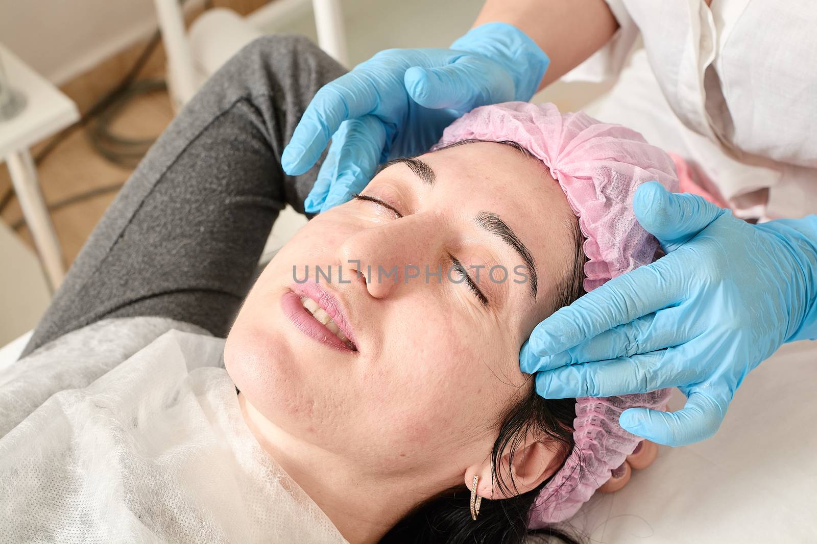 Young woman does professional facial massage after moisturizing, softening, regenerating, rejuvenating, toning cosmetic procedures in the beauty salon. Close-up view.