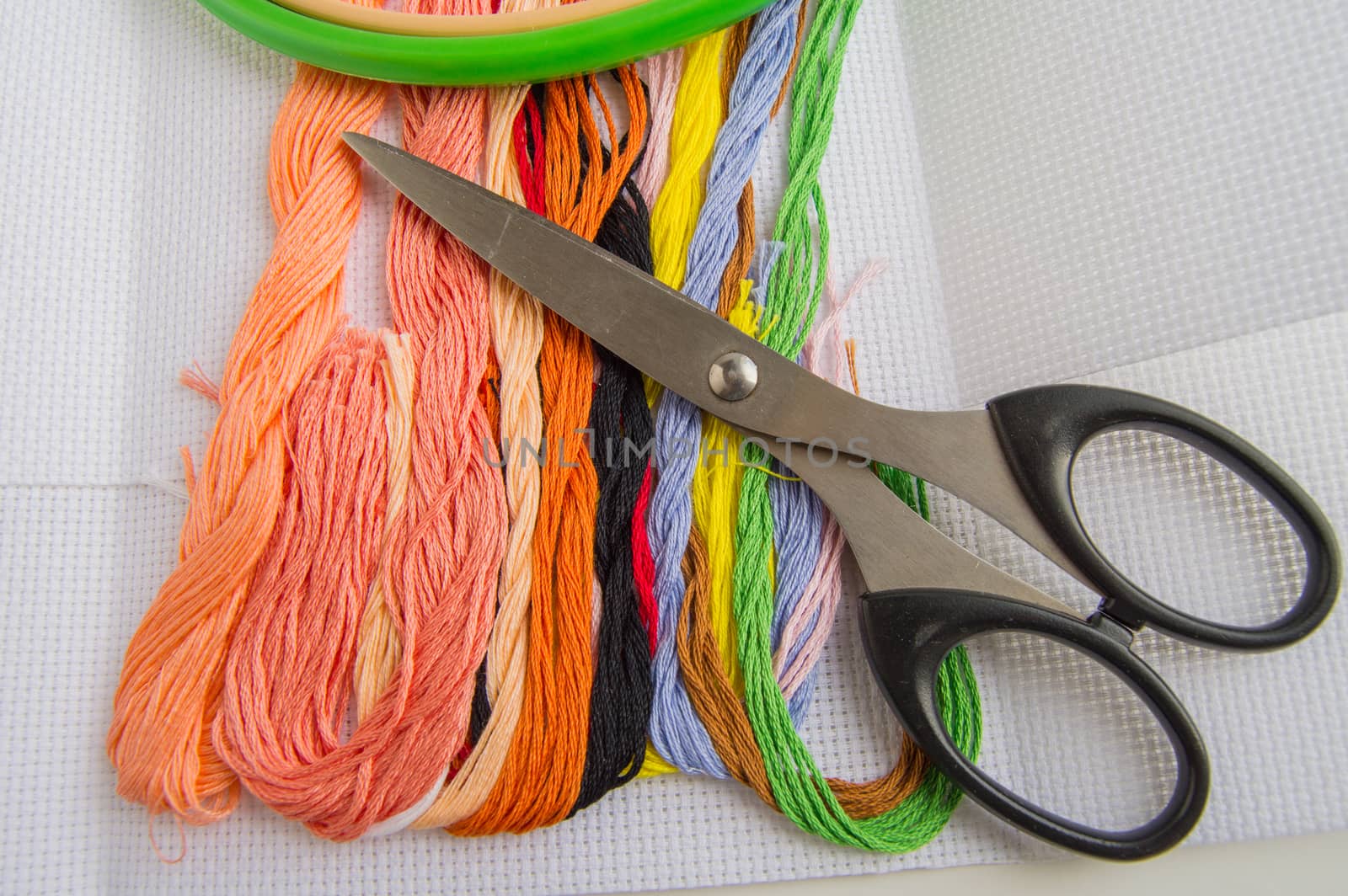 Scissors and bright colorful thread for embroidery thread on canvas. Handmade accessories on white background. Place for text, top view.