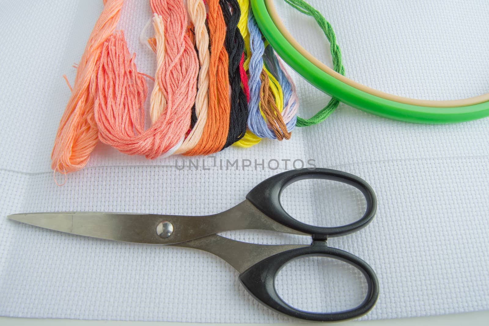 Scissors and bright colorful thread for embroidery thread on canvas. Handmade accessories on white background. Place for text, top view.