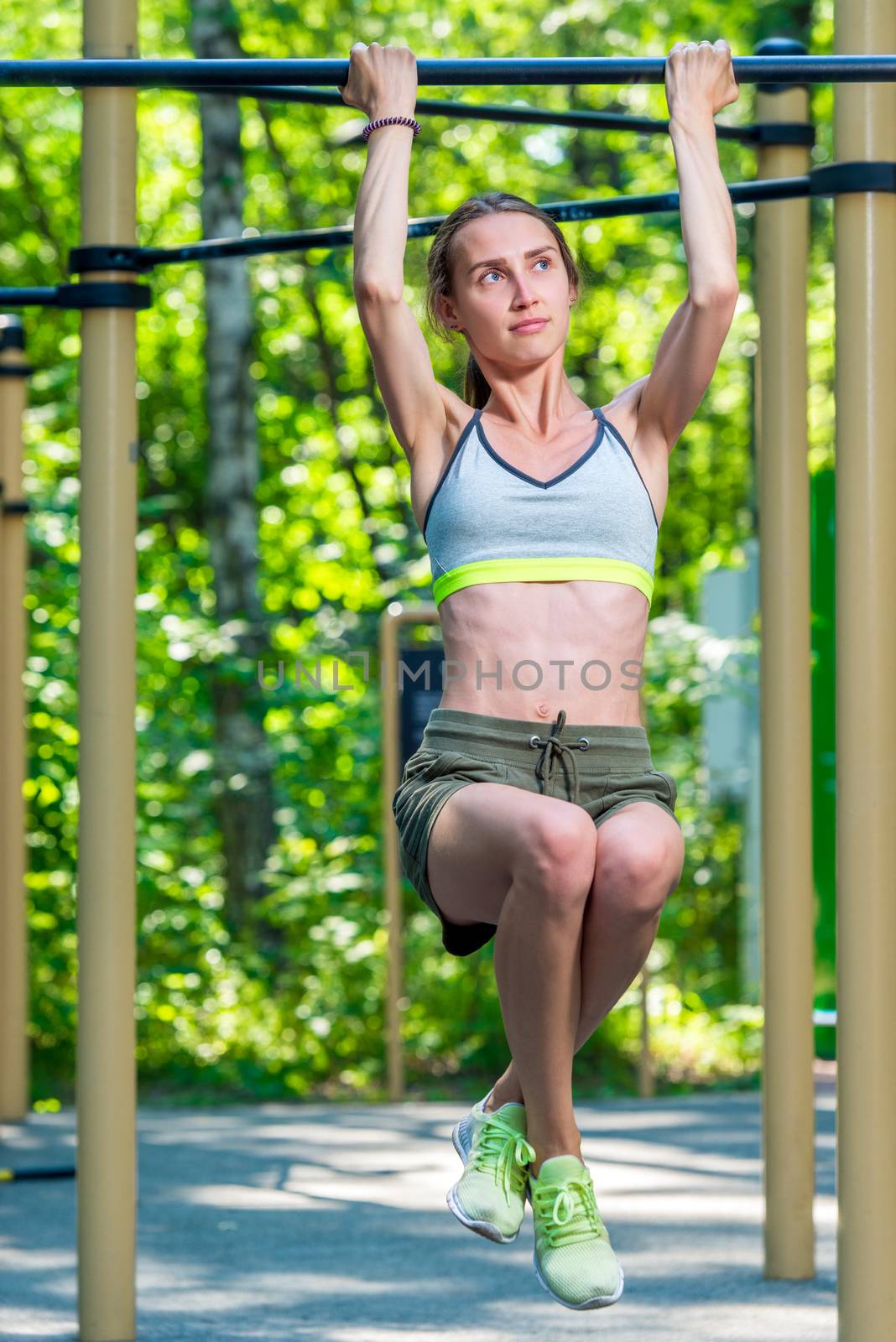 muscular woman on the crossbar doing exercises in the park by kosmsos111