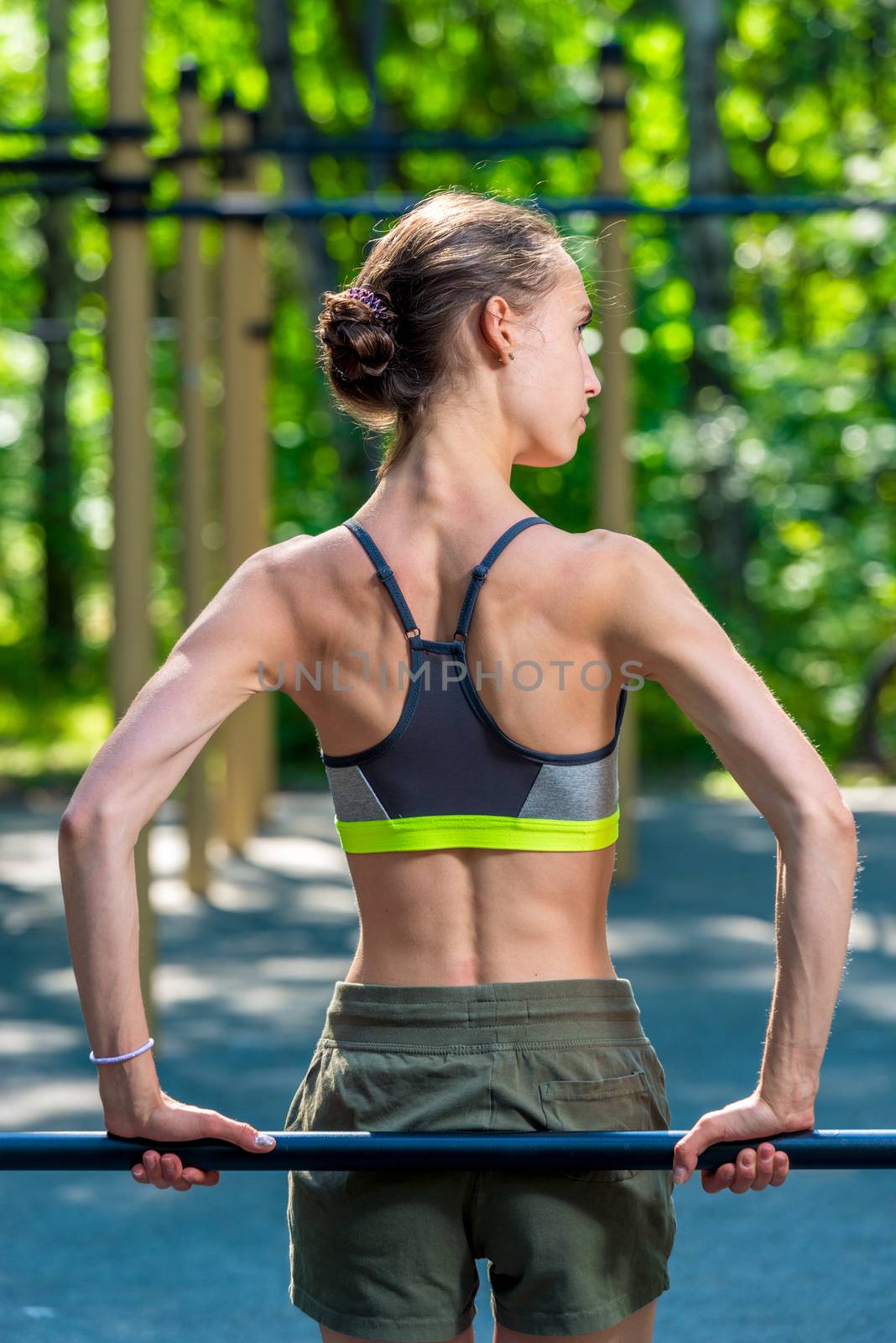 portrait from the back girl with a muscular figure, who is engaged on the playground outside in the park