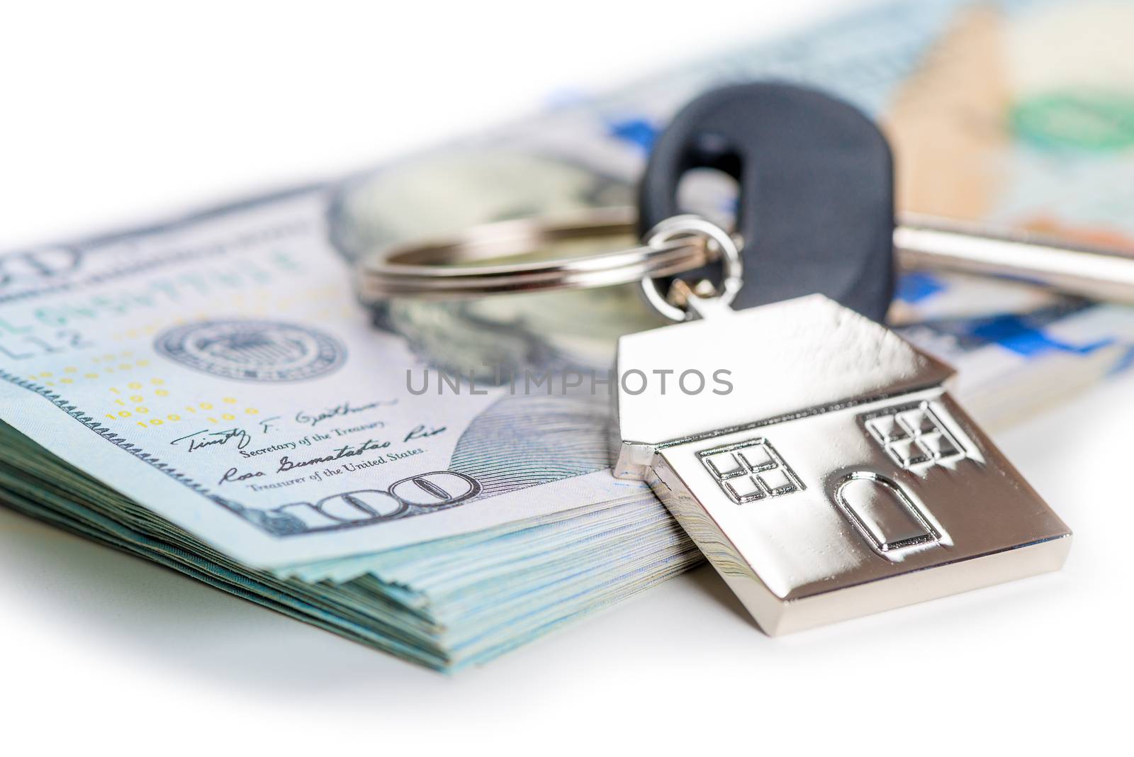 on white background close up of house key on pile of american dollars