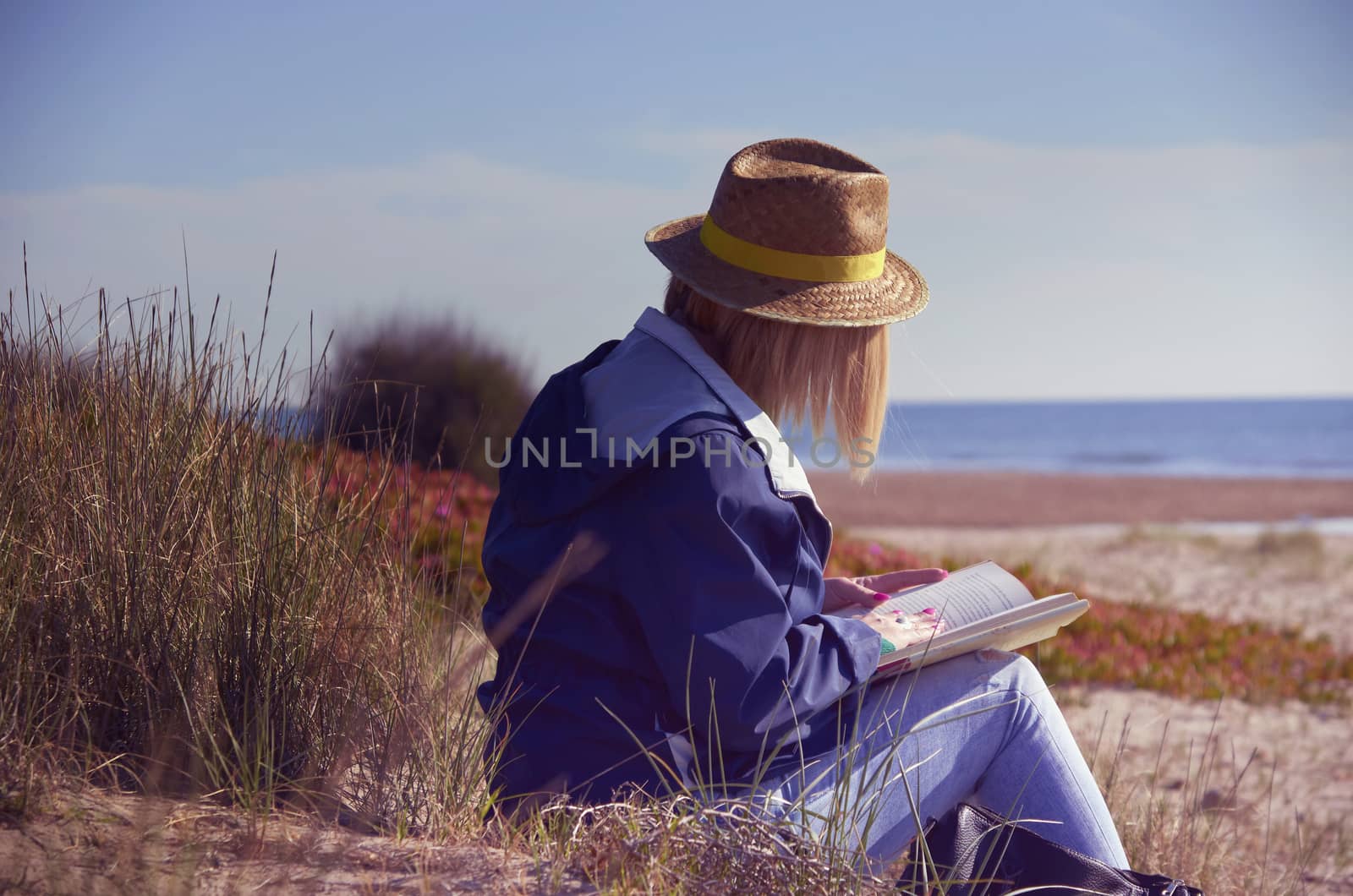 Woman sitting in the sun on the beach reading a book glam-our color