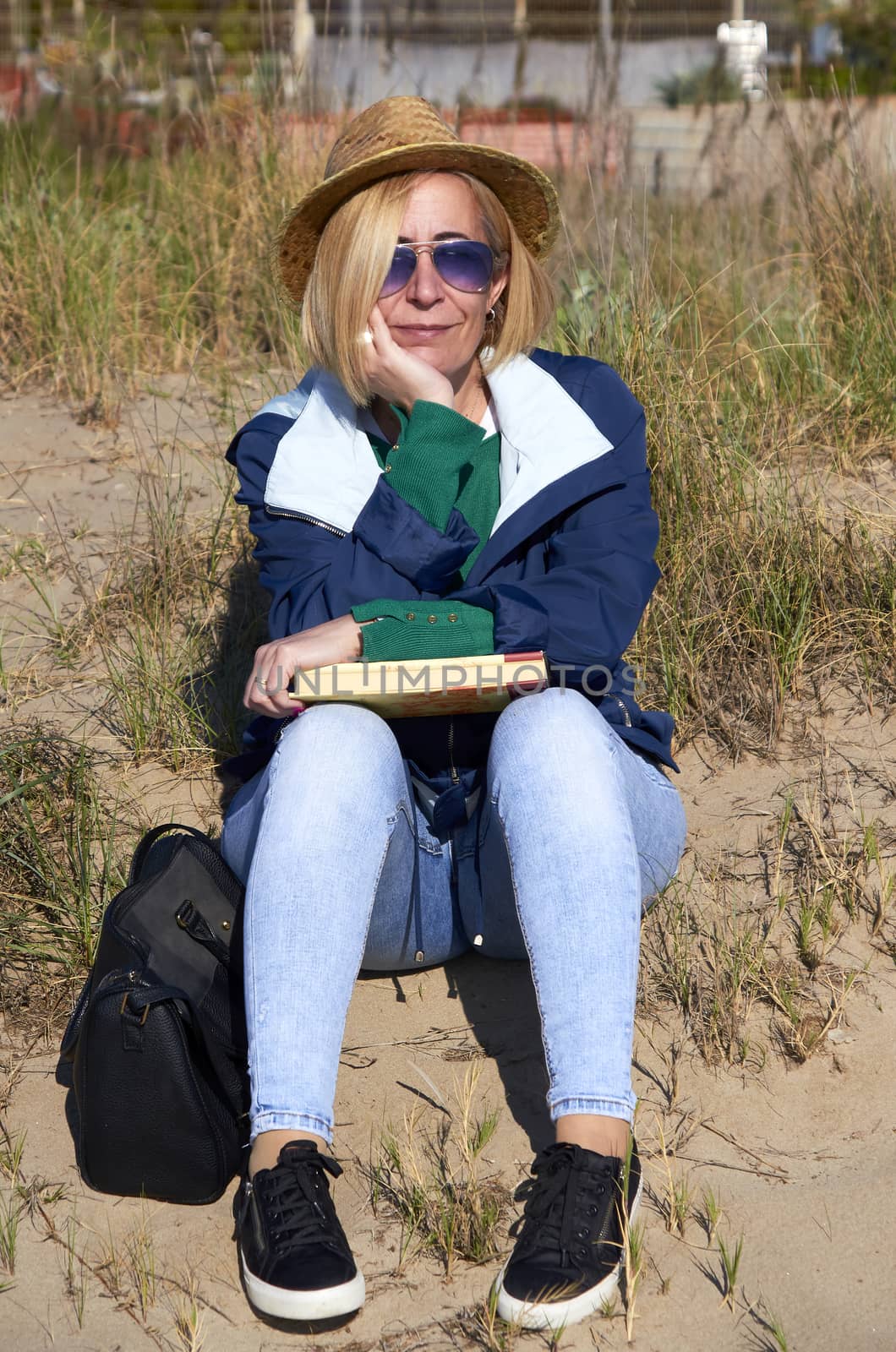 Woman sitting in the sun on the beach reading a book