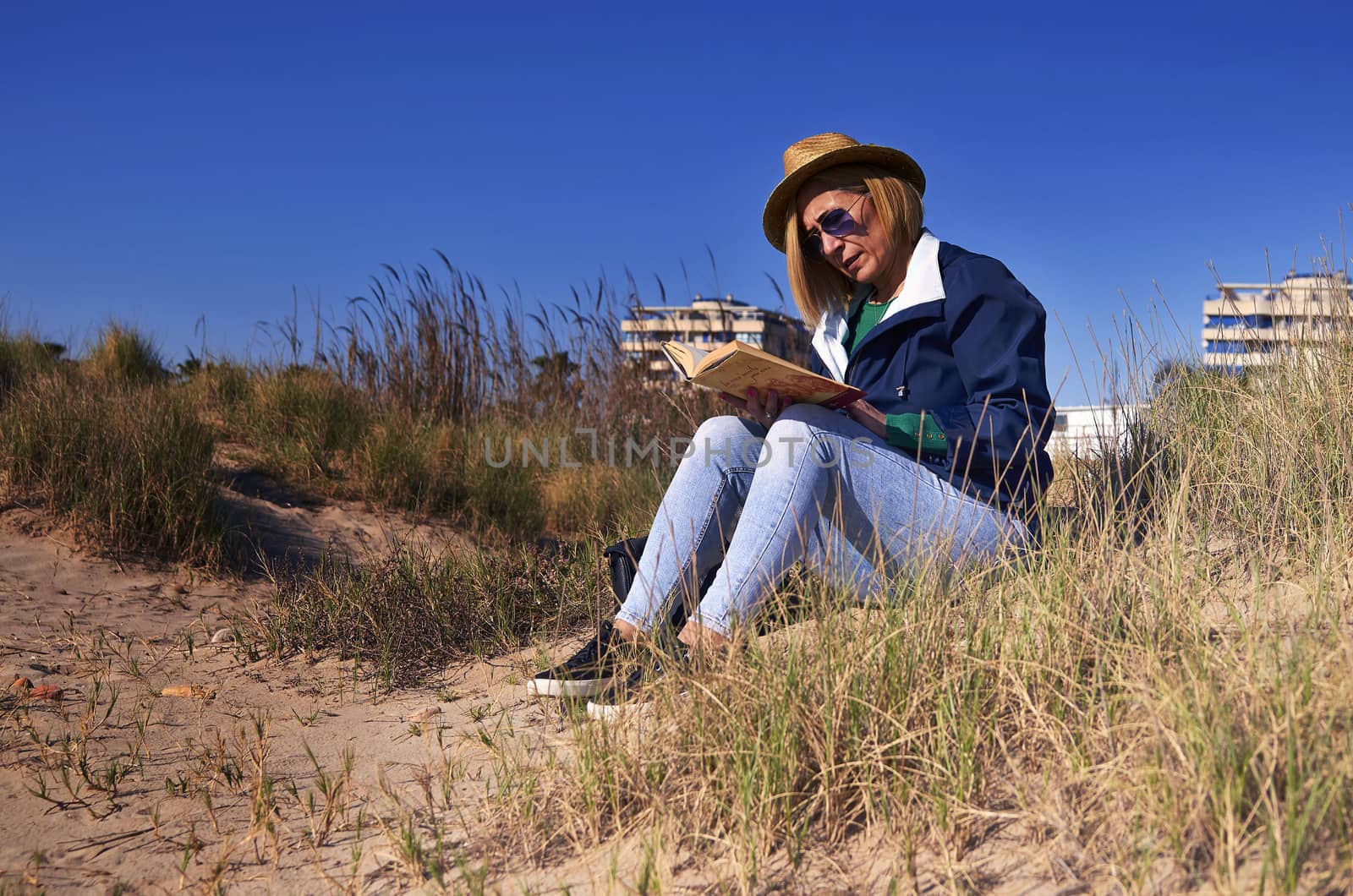 Woman sitting in the sun on the beach reading a book