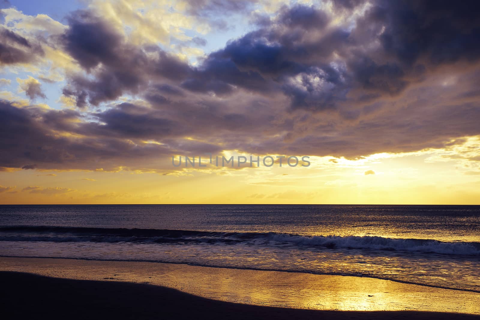 colorful sunset on the beach, the blue sky is covered in clouds and it is orange and yellow on the horizon