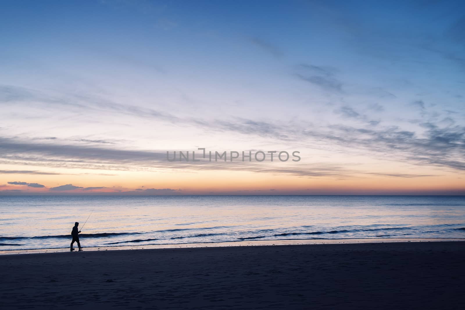 silhouette of a man walking with his fishing rod by the seashore during a spectacular sunset in Chiclana, Cadiz, Andalusia, Spain