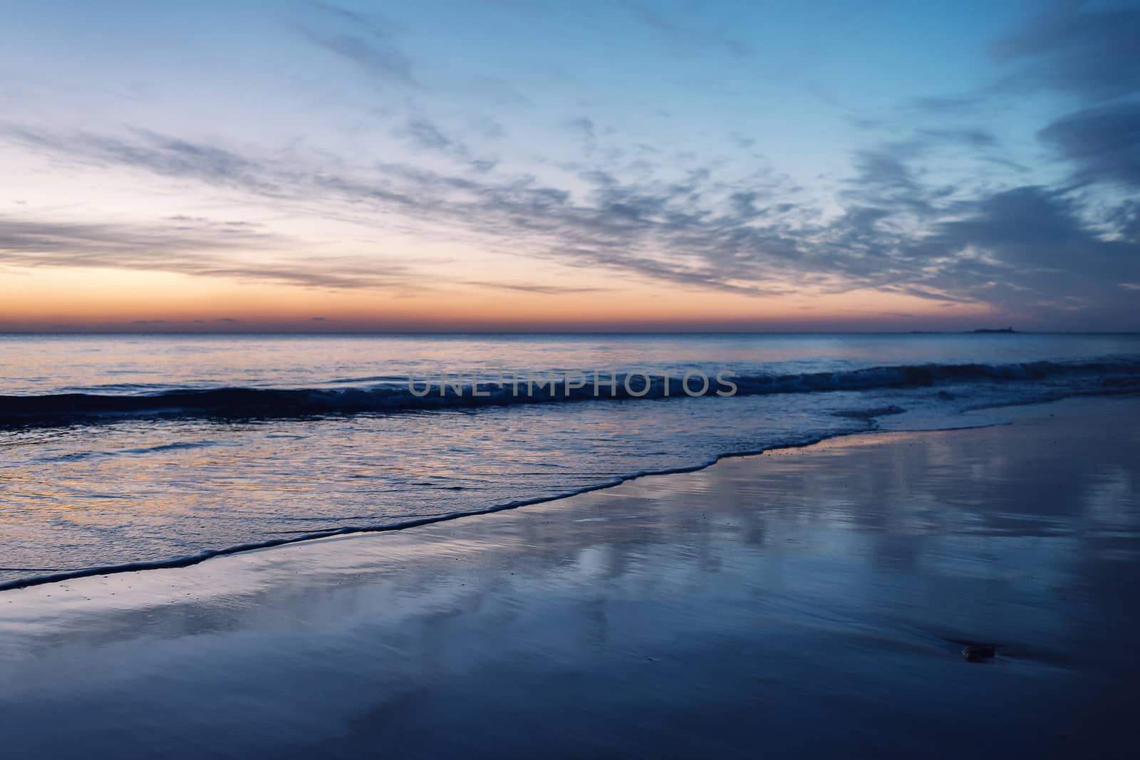 beautiful sunset on a lonely beach, the wet sand of the beach reflects the blue sky and the orange light of the horizon