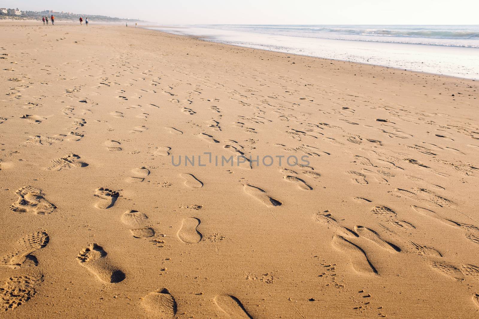 footprints in the wet sand of the beach, in the background there are people walking along the shore