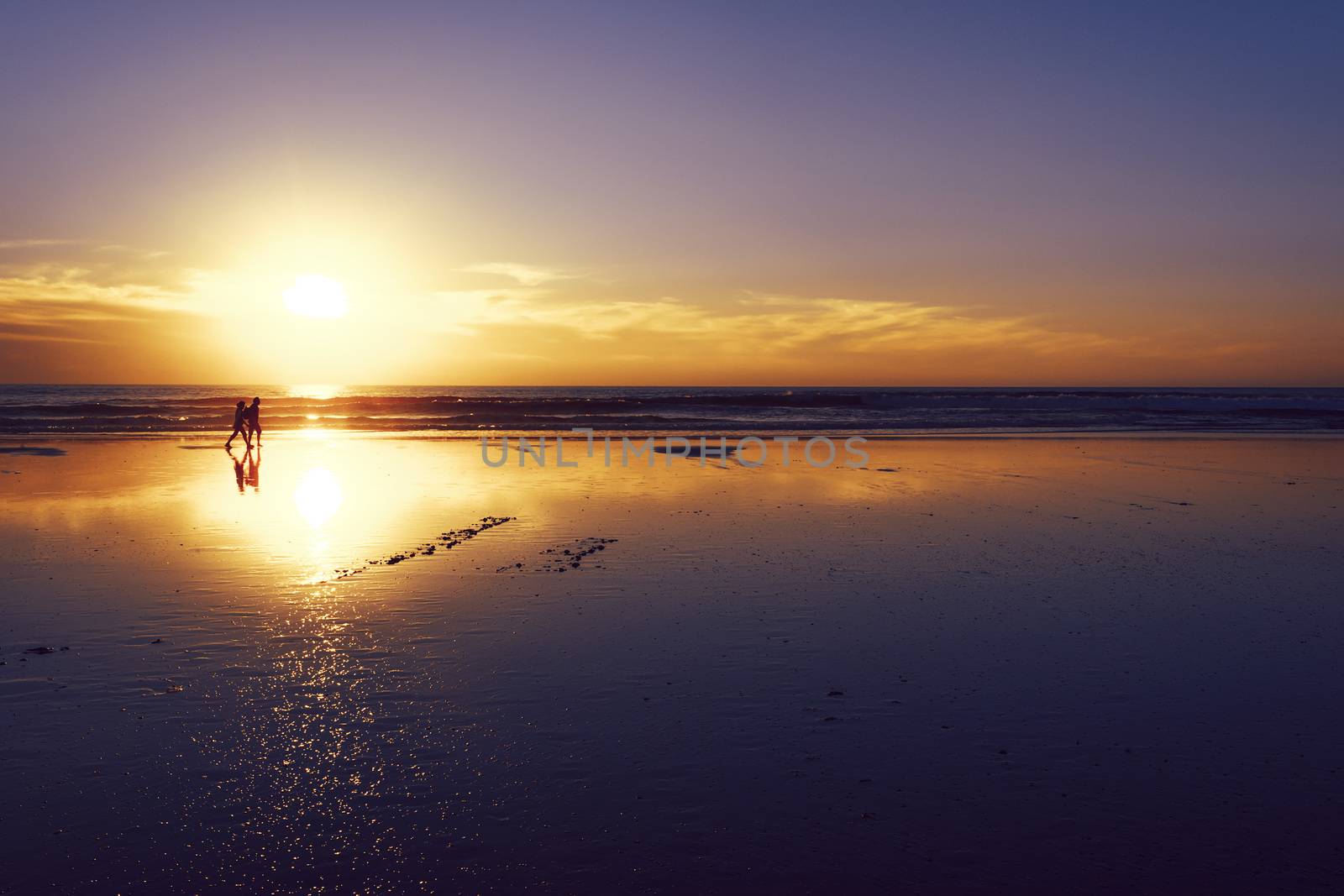 silhouette of a couple strolling on the beach, walk at sunset over the reflection of the sun on the wet sand