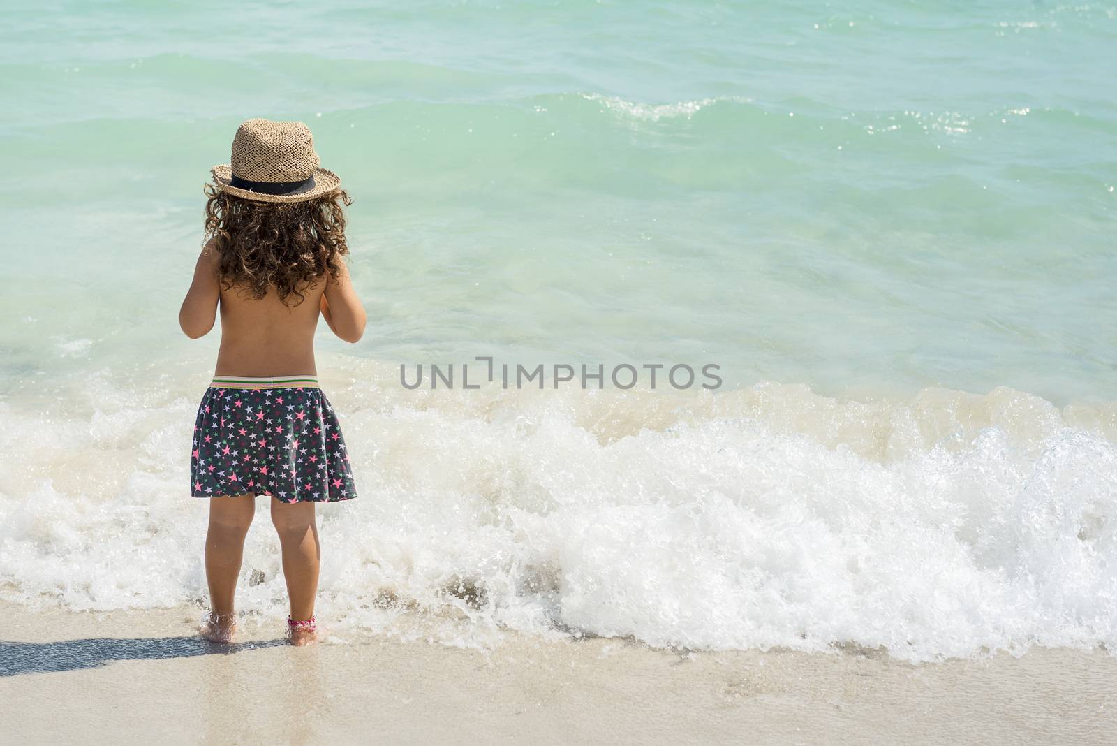 little girl with her back on the shore of a paradisiacal beach of white sand and turquoise waters, wearing a skirt and a cane hat