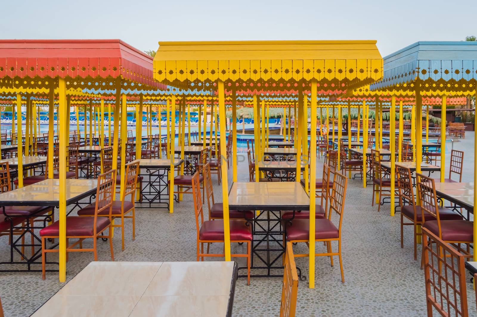 Outdoor wooden restaurant terrace with tables with four seats with a small roof against the sun.