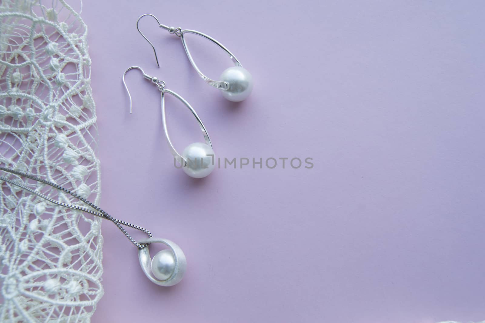 Beautiful silver shiny pearl jewelry, trendy glamorous earrings, chain on pink purple background with exquisite lace. Flat lay, top view, copy location.