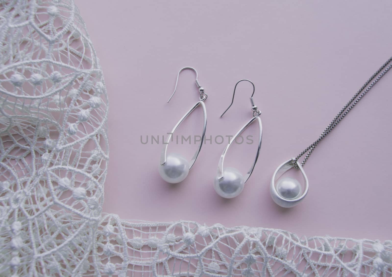 Beautiful silver shiny pearl jewelry, trendy glamorous earrings, chain on pink purple background with exquisite lace. Flat lay, top view, copy location.