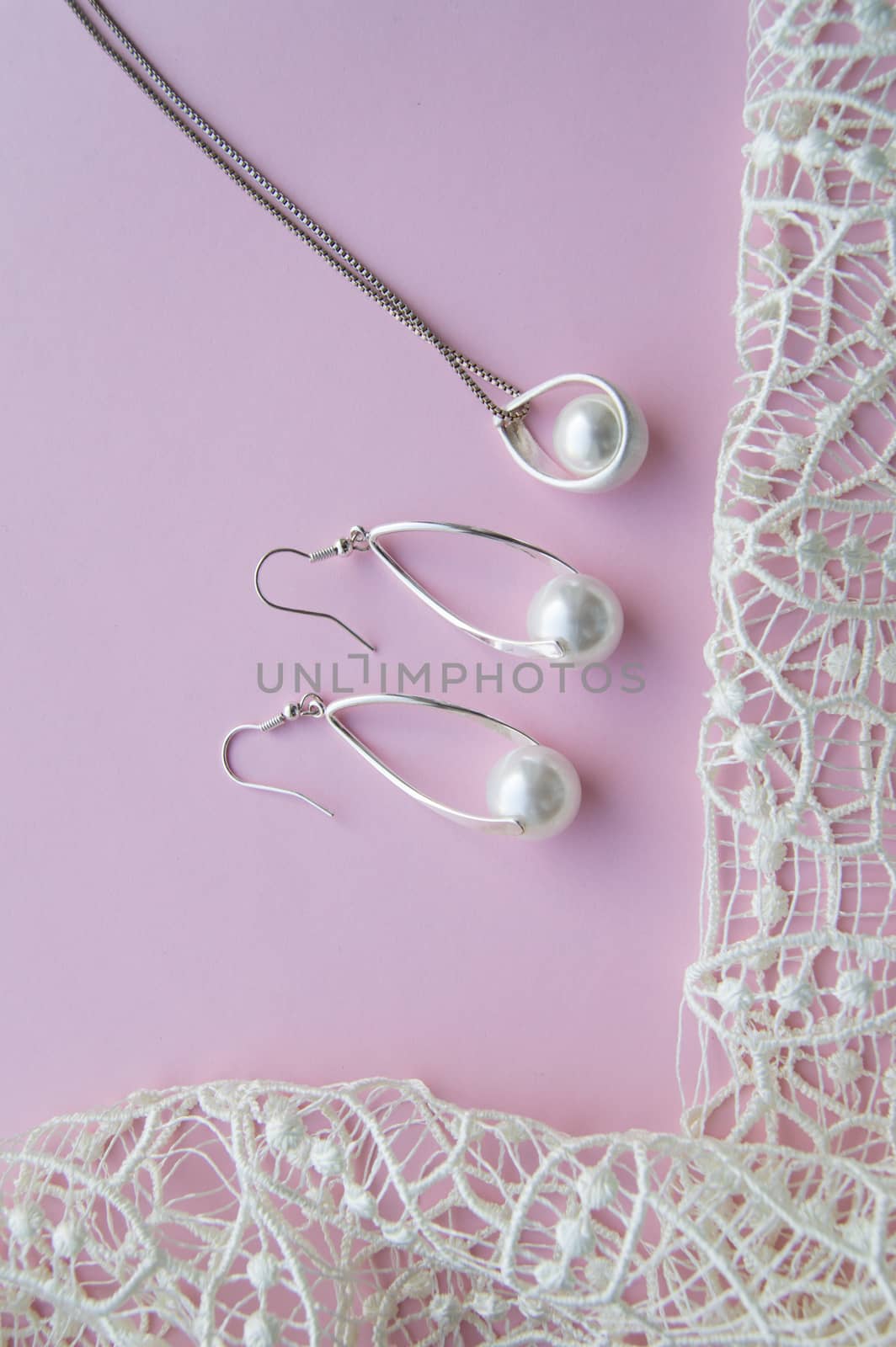 Beautiful silver shiny pearl jewelry, trendy glamorous earrings, chain on pink purple background with exquisite lace. Lay Flat, top view, copy the location of the vertical frame