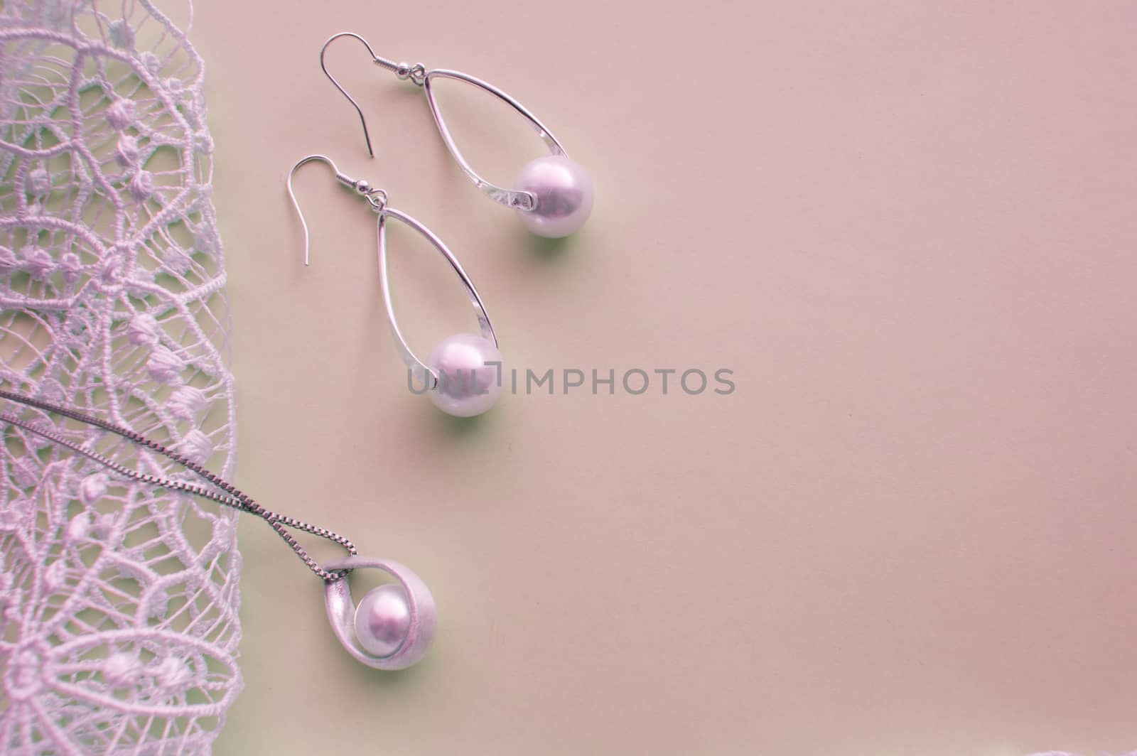 Beautiful silver shiny pearl jewelry, trendy glamorous earrings, chain on pink purple background with exquisite lace. Flat lay, top view, copy location.