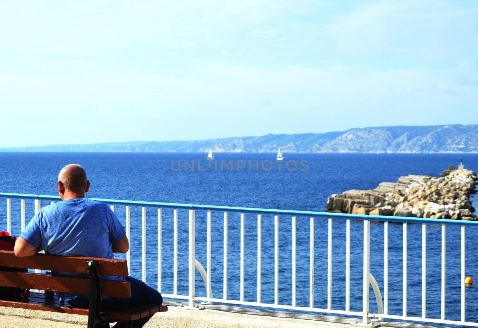 A young man traveler sitting on a bench on Mediterranean coast on promenade of Marseille. Back view of beautiful sea panorama and sailboats by claire_lucia