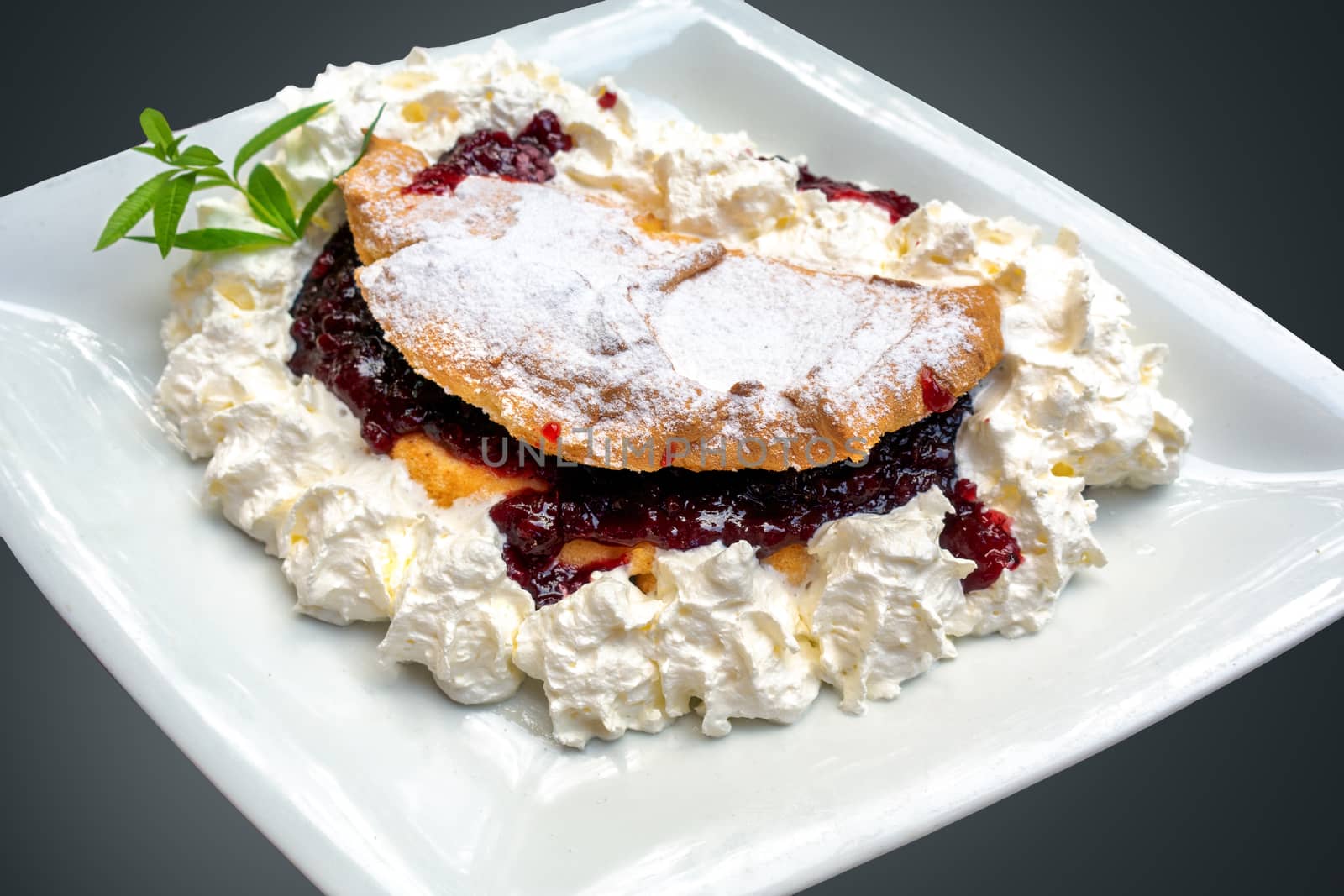 Fruit omelet with cranberry jam, powder sugar and whipped cream on white plate, with green herbs, isolated on grey background, traditional European dessert known as Pohorska omleta, Pohorje omelette