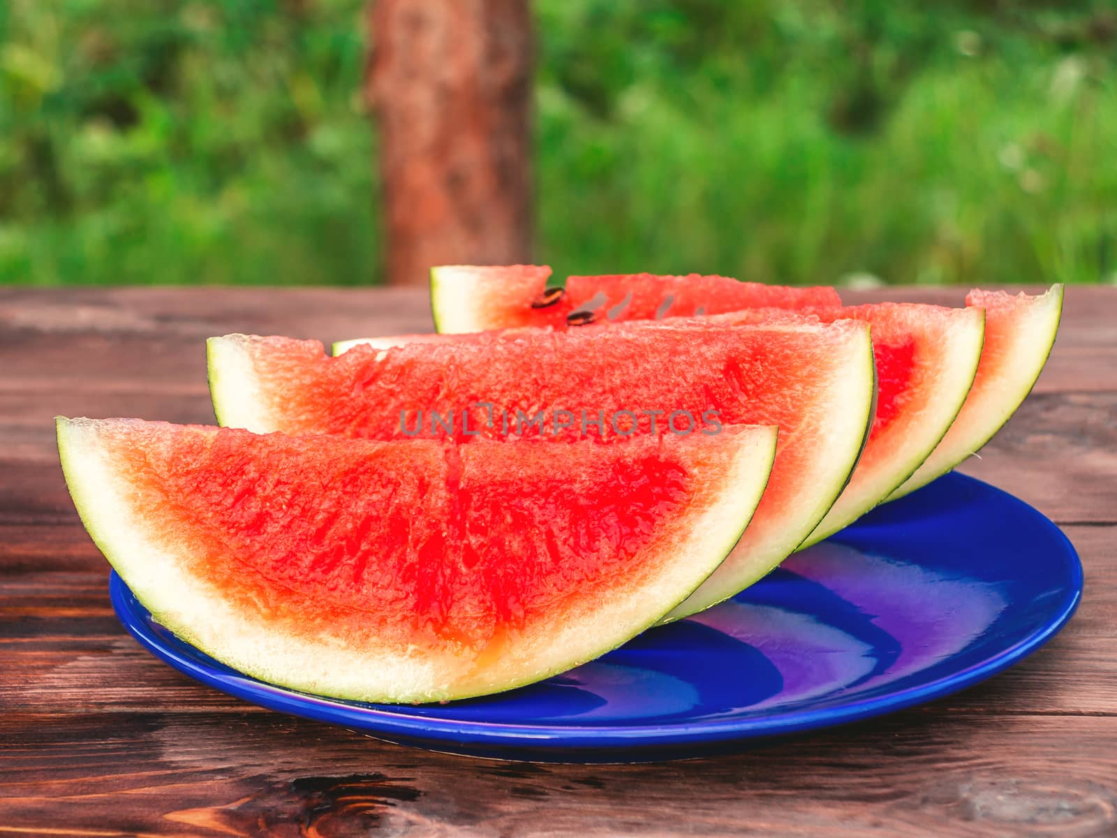 Sliced ripe red watermelon on a blue plate on a wooden table.