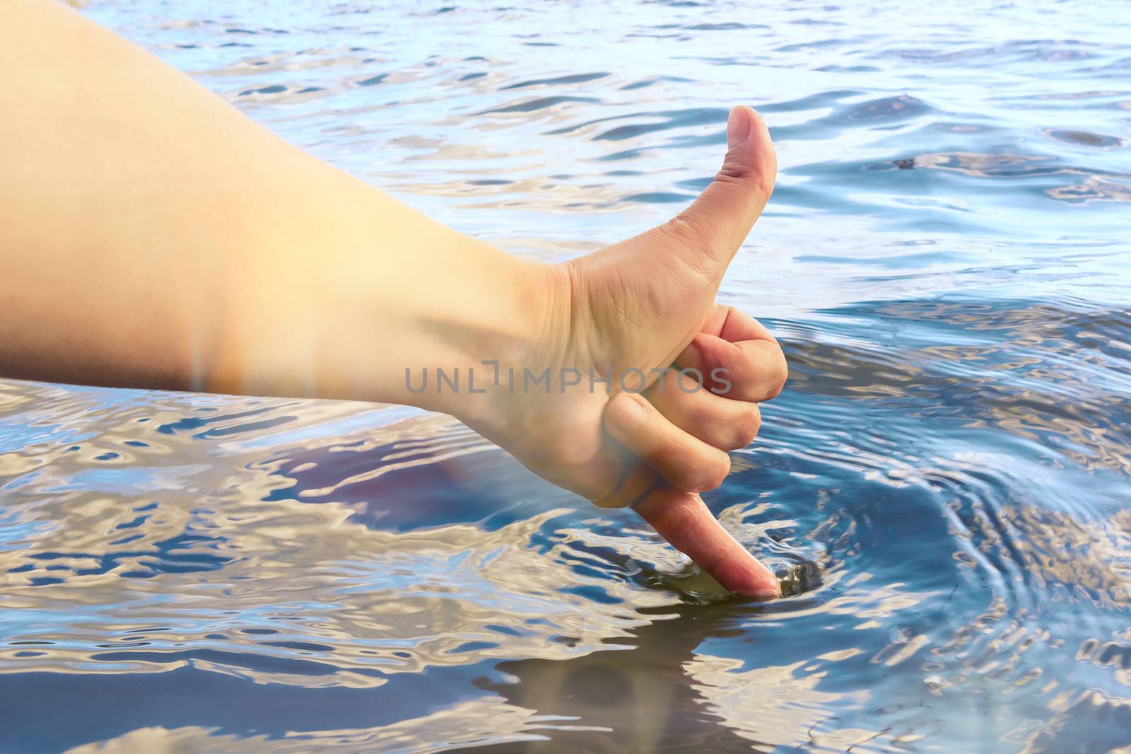 Female hand touches the water with a finger and shows that it is warm and clean. Summer vacation and swimming concept.