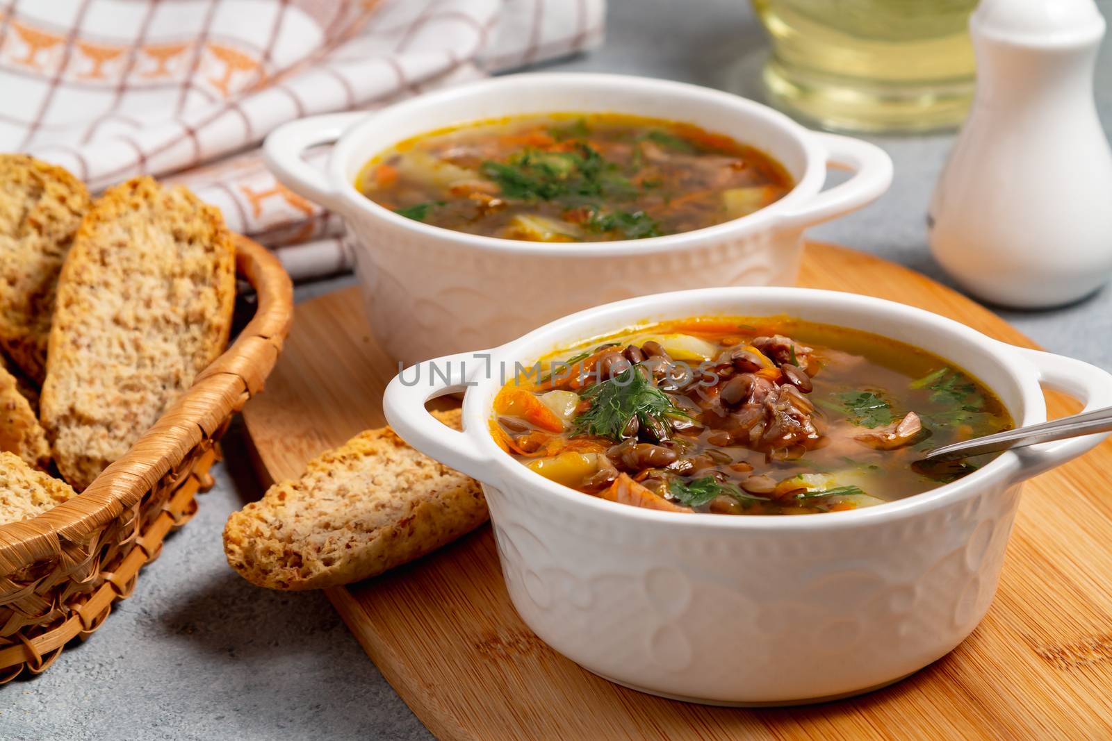 Two plates with lentil soup and chicken on a wooden board on black table by galsand