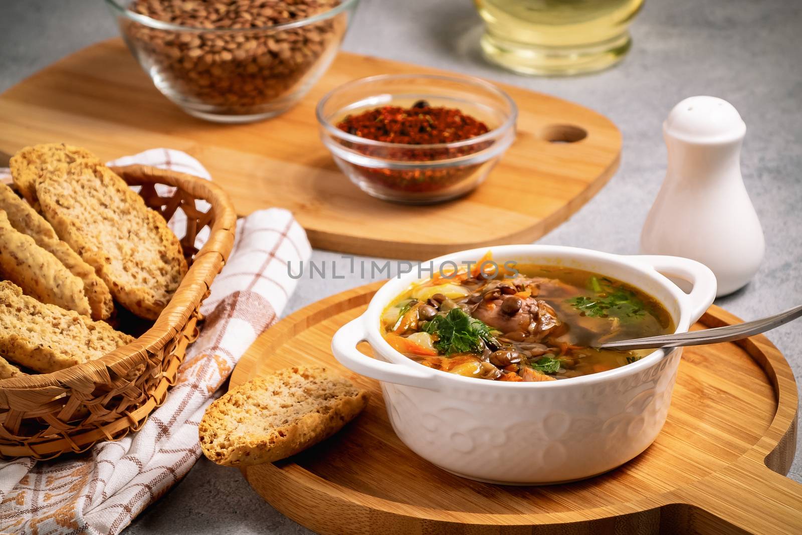 Lentil soup with chicken in a white bowl on a wooden board on a gray table and ingredients by galsand