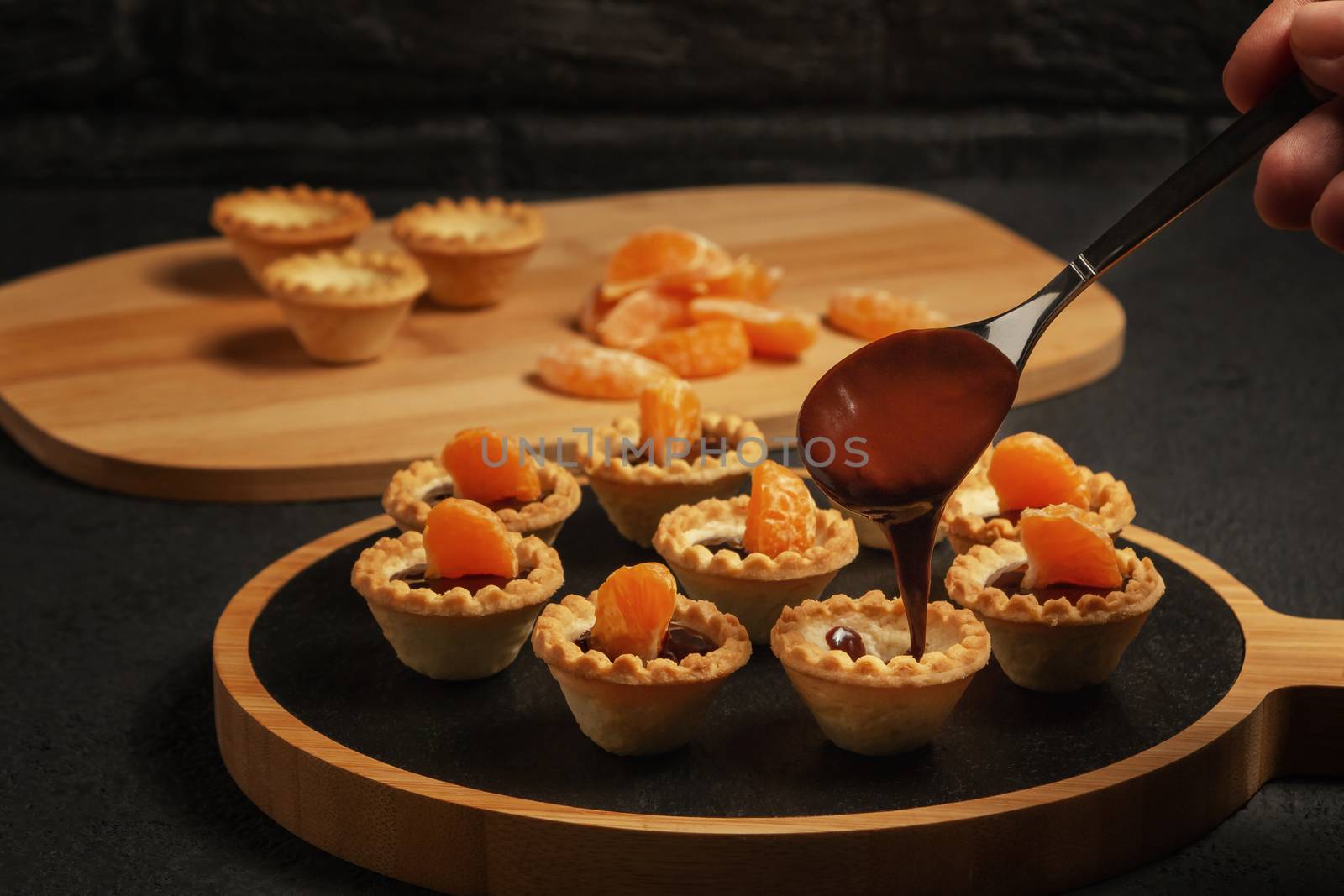 Cooking sweet tartlets with tangerine slices - pouring melted chocolate.
