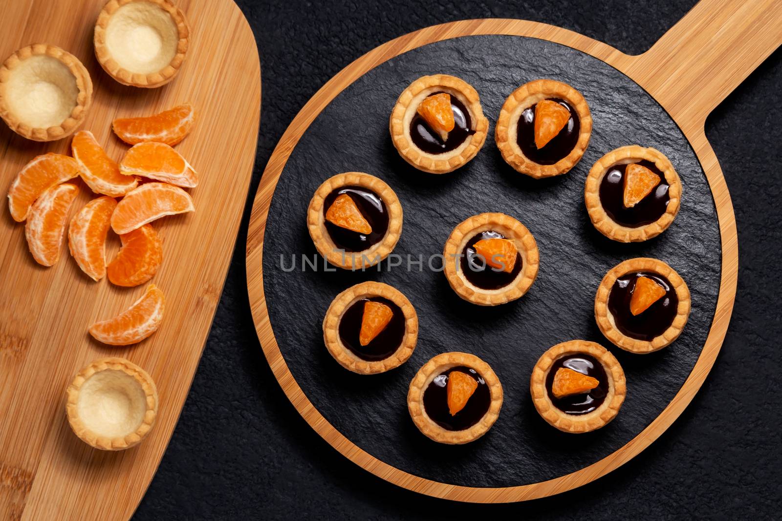 Sweet tartlets with chocolate and slices of tangerine on a dish of natural slate for serving, top view.