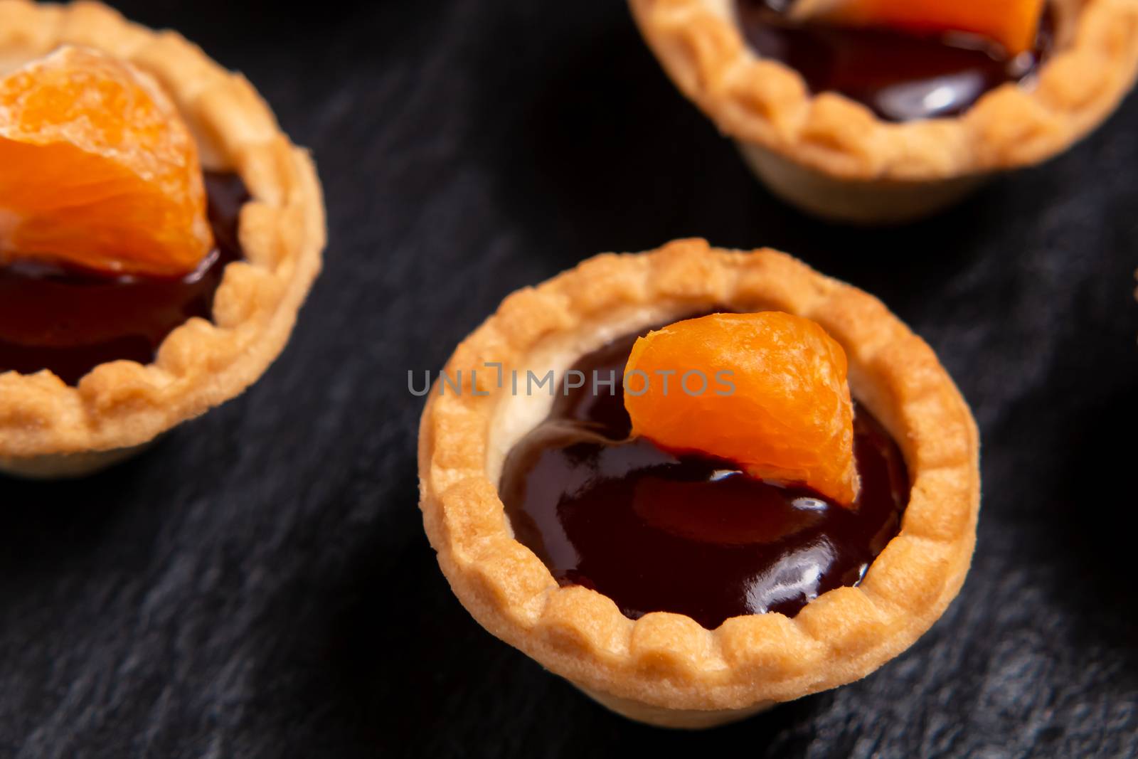 Sweet tartlets with chocolate and slices of tangerine on a dish of natural slate for serving, close-up by galsand