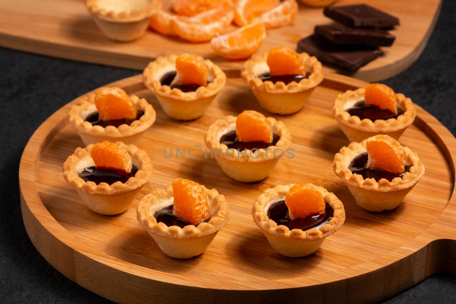 Sweet tartlets with chocolate and slices of tangerine on a wooden dish for serving.