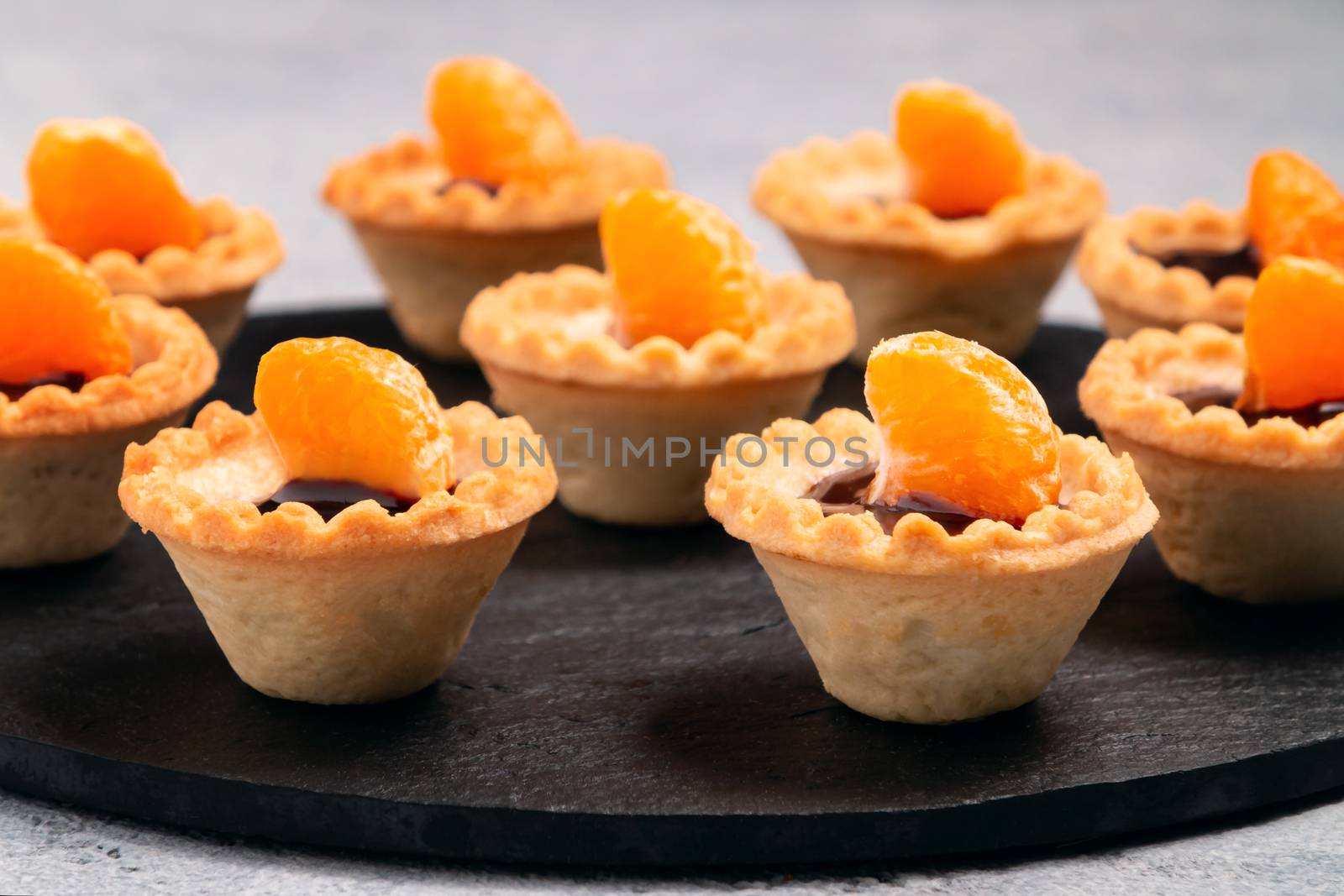 Sweet tartlets with chocolate and slices of tangerine on a dish of natural slate for serving by galsand