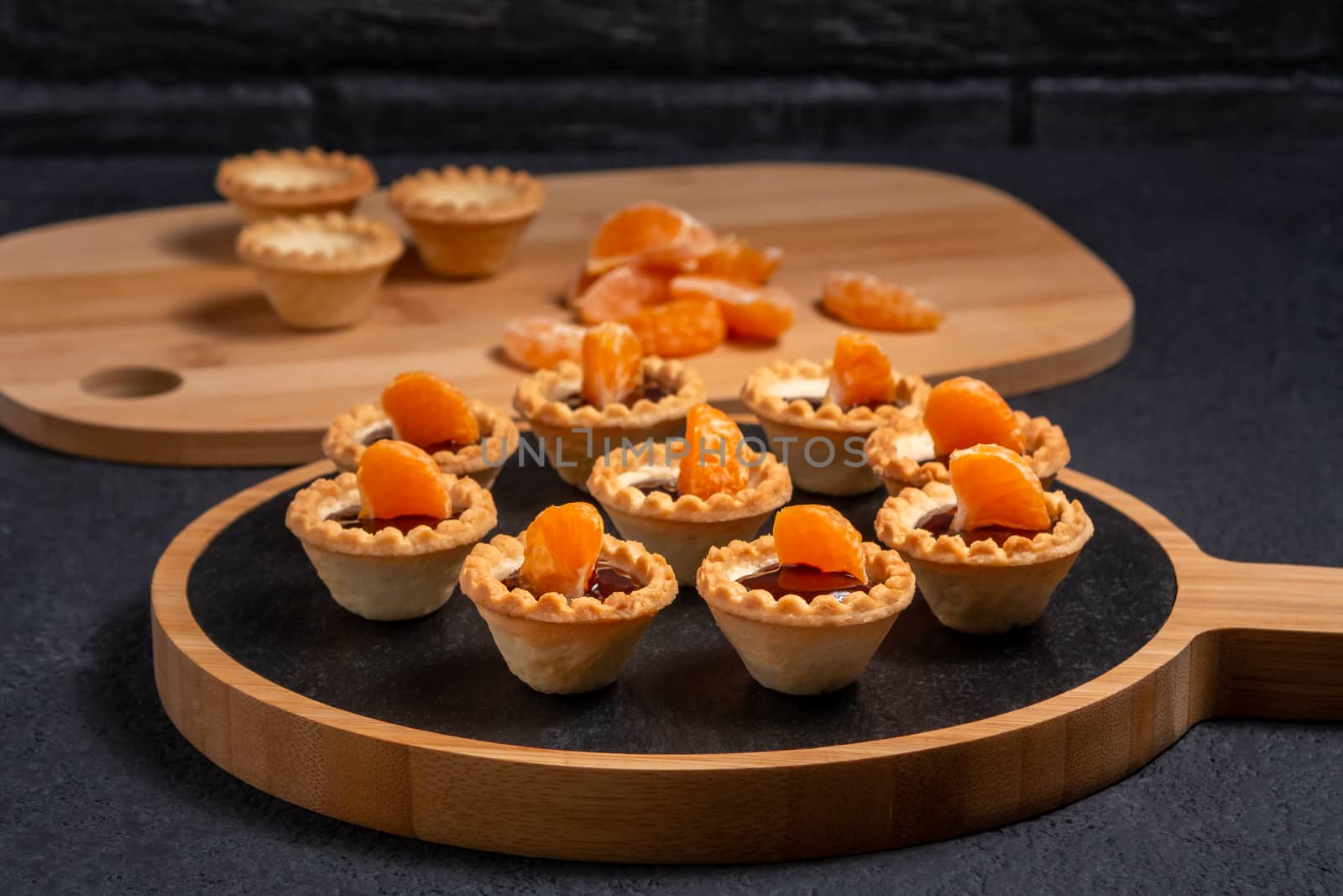 Sweet tartlets with chocolate and slices of tangerine on a dish of natural slate for serving.