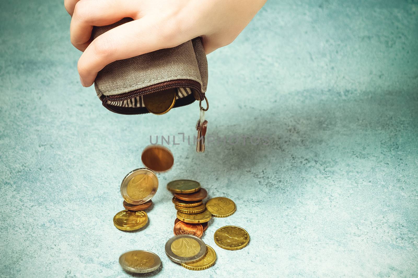 Several coins fall on the table from an empty wallet in a woman's hand, poverty, crisis, bankruptcy and financial problems concept by galsand