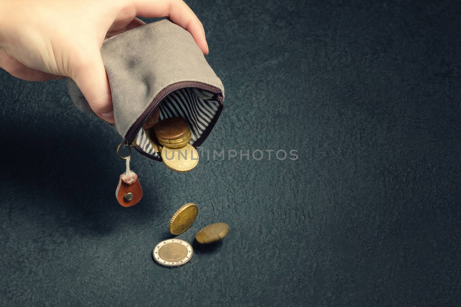 Several coins fall on the table from an empty wallet in a woman's hand, poverty, crisis, bankruptcy and financial problems concept.