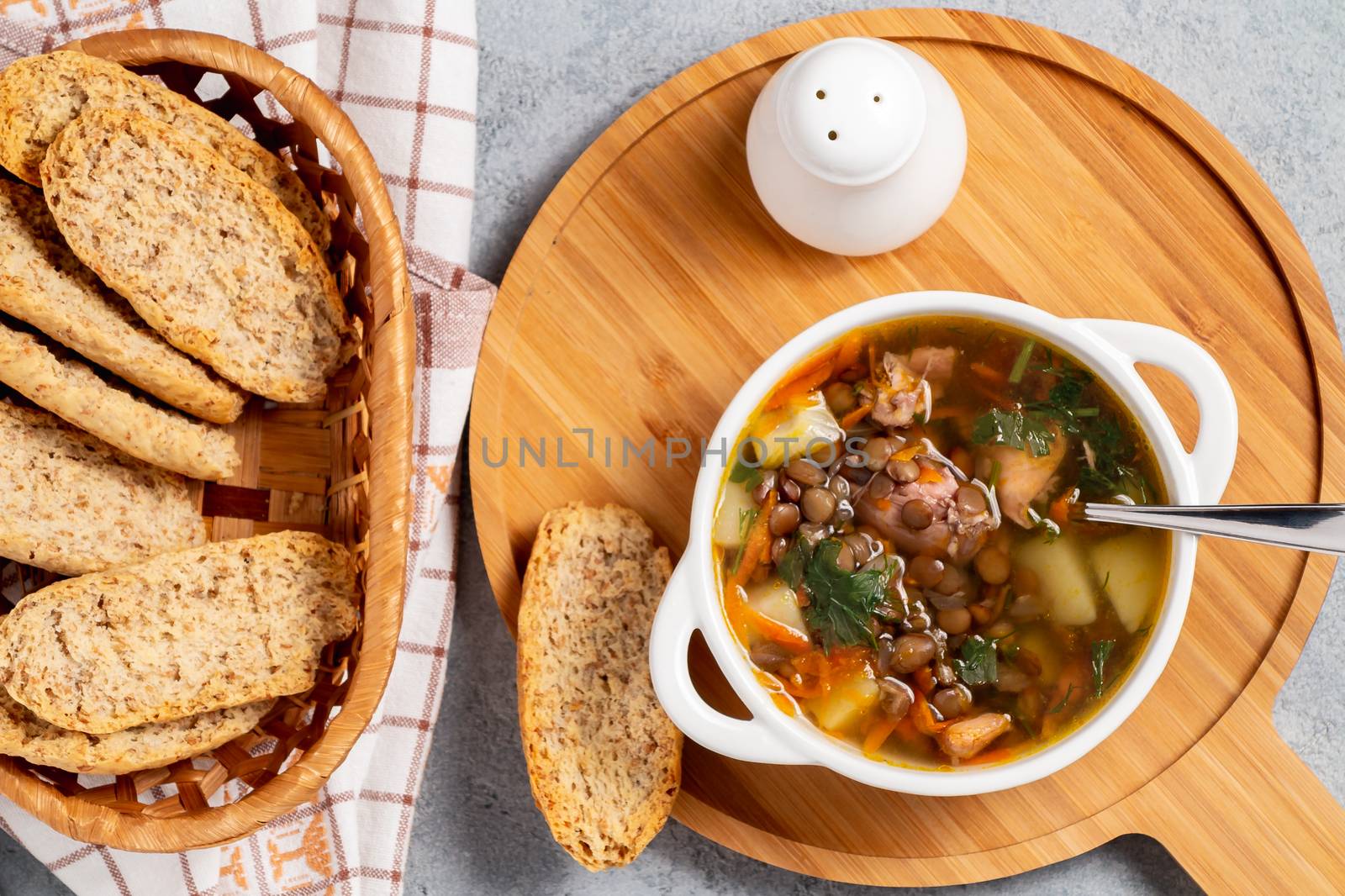 Lentil soup with chicken in a white bowl on a wooden board on a gray table, top view.