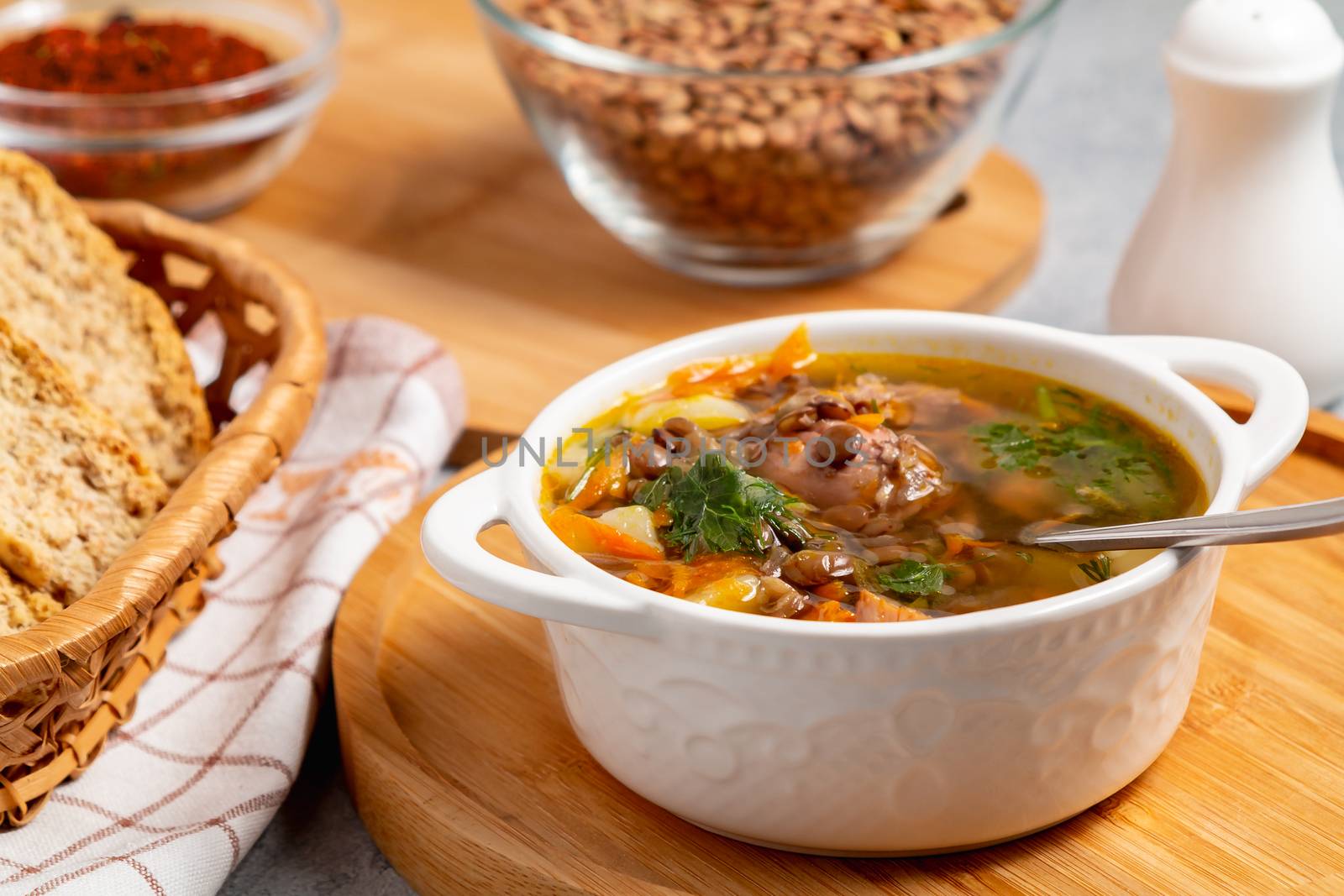 Lentil soup with chicken in a white bowl on a wooden board.