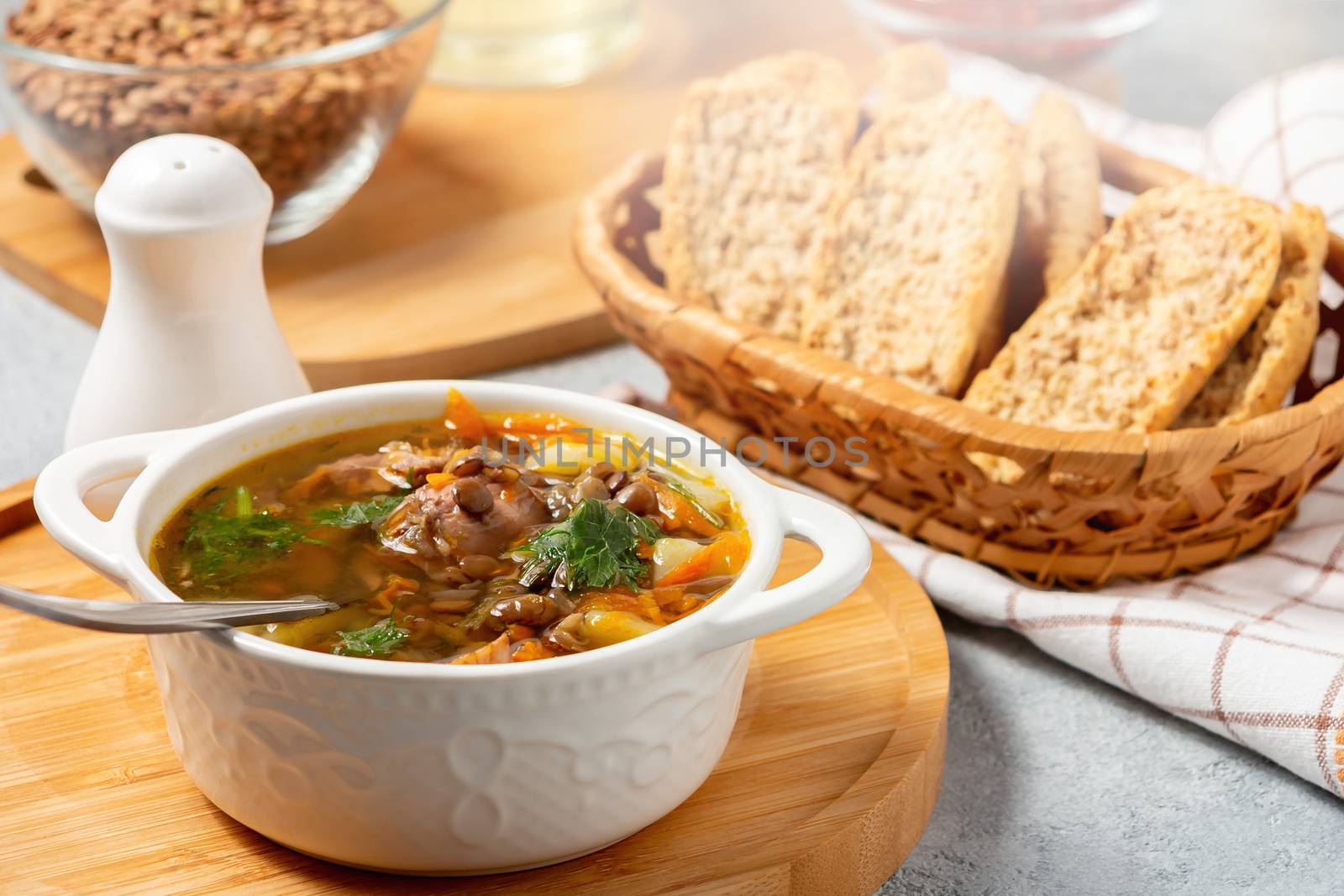Lentil soup with chicken in a white bowl on a wooden board.