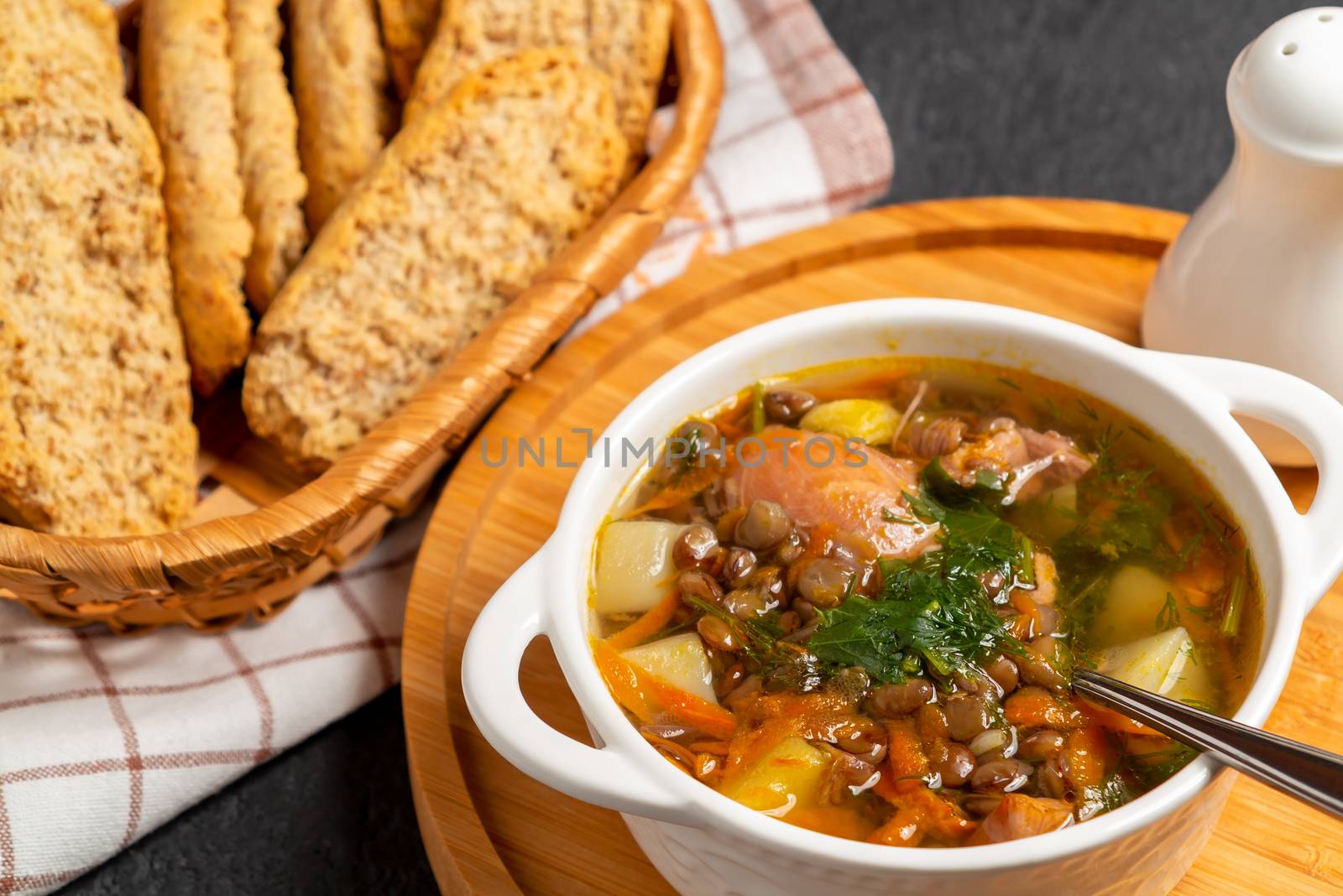 Lentil soup with chicken in a white bowl on a wooden board on a black table.
