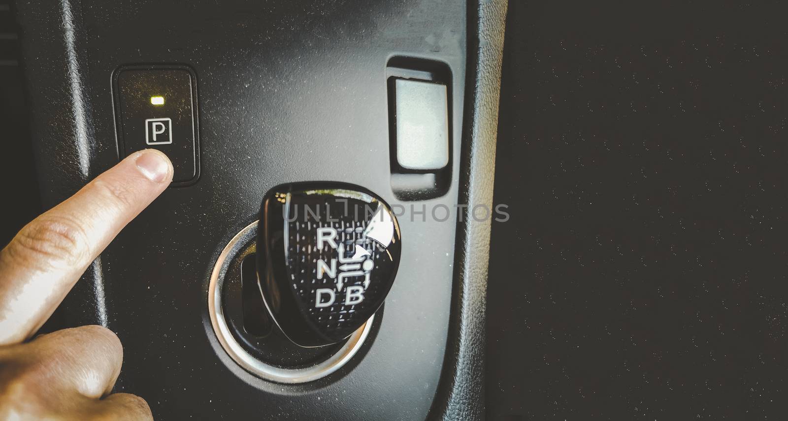 hand finger press park gear button on automatic transmission car interior overhead above view horizontal background film grain by LucaLorenzelli