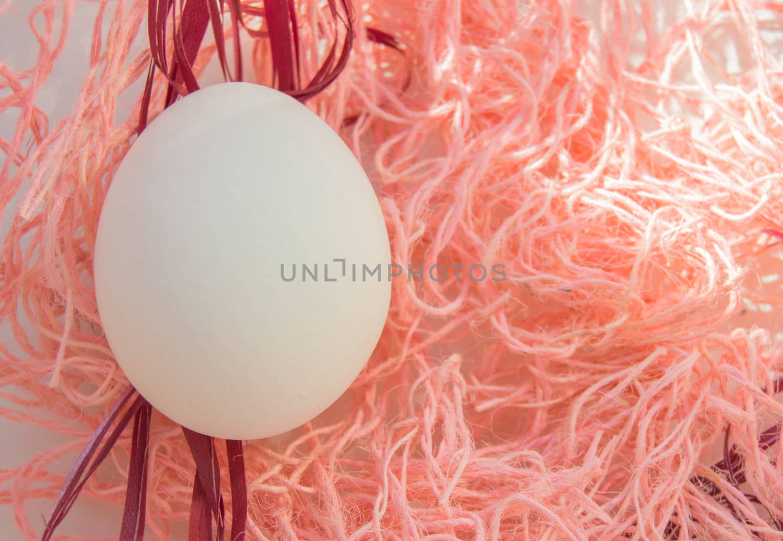 Easter concept, white egg on pink background, woven fabric nest, top view, copy space, bright sunlight