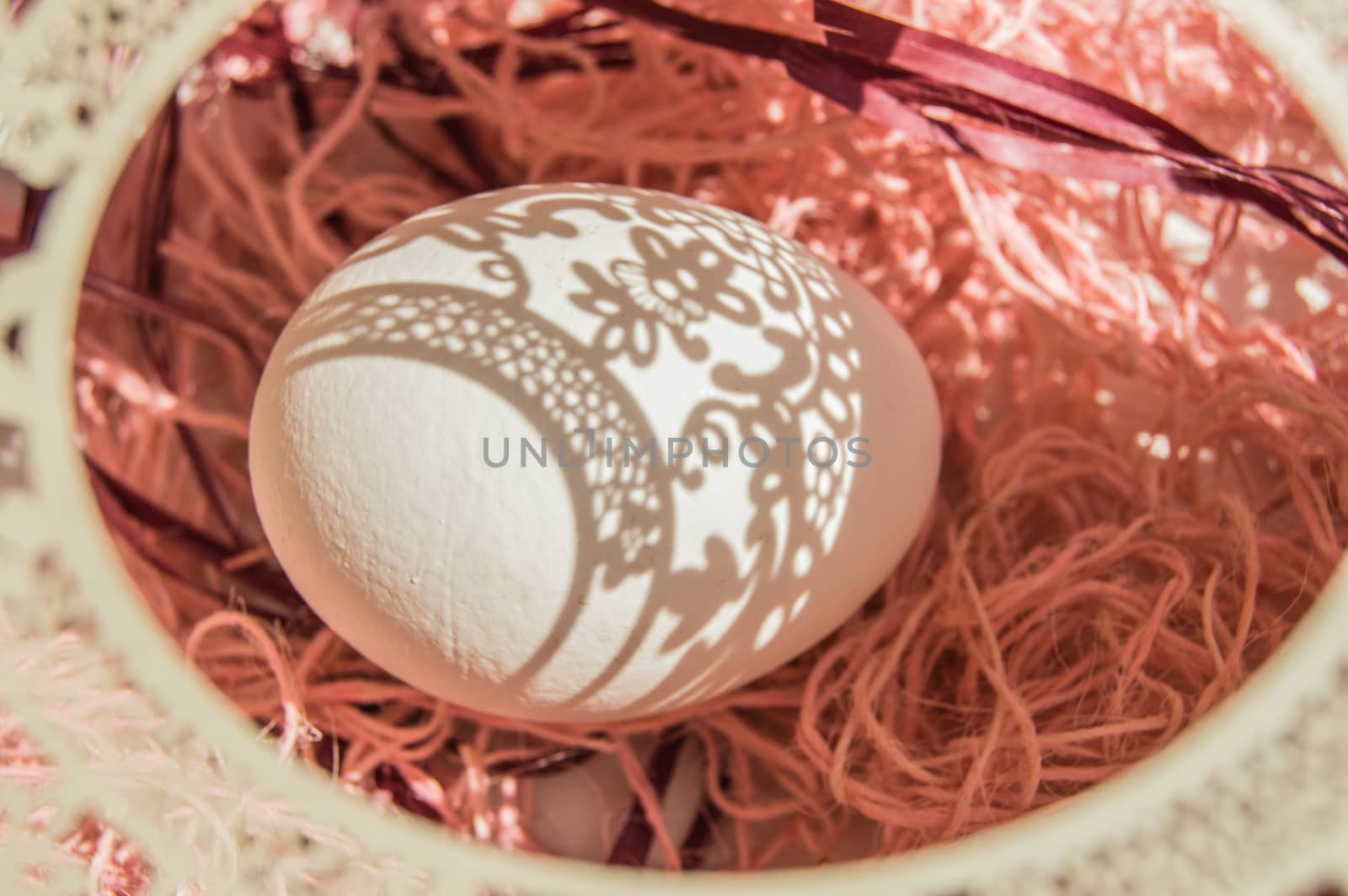 Easter card with egg and white openwork oval frame on coral background, Bright sunlight creates beautiful shadows on white egg, copyspace, top view